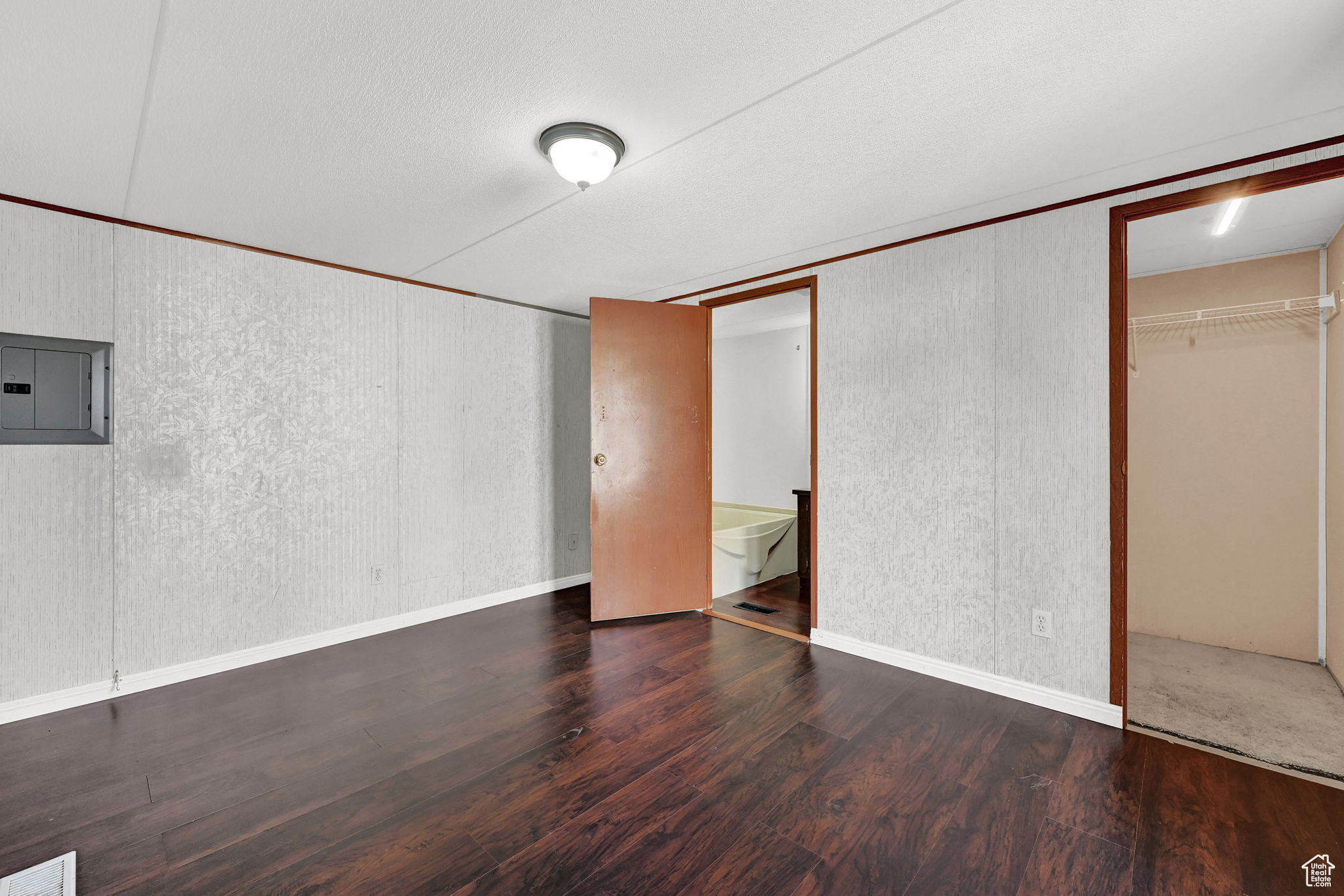 Unfurnished bedroom with ensuite bathroom, a textured ceiling, dark wood-type flooring, electric panel, and a closet