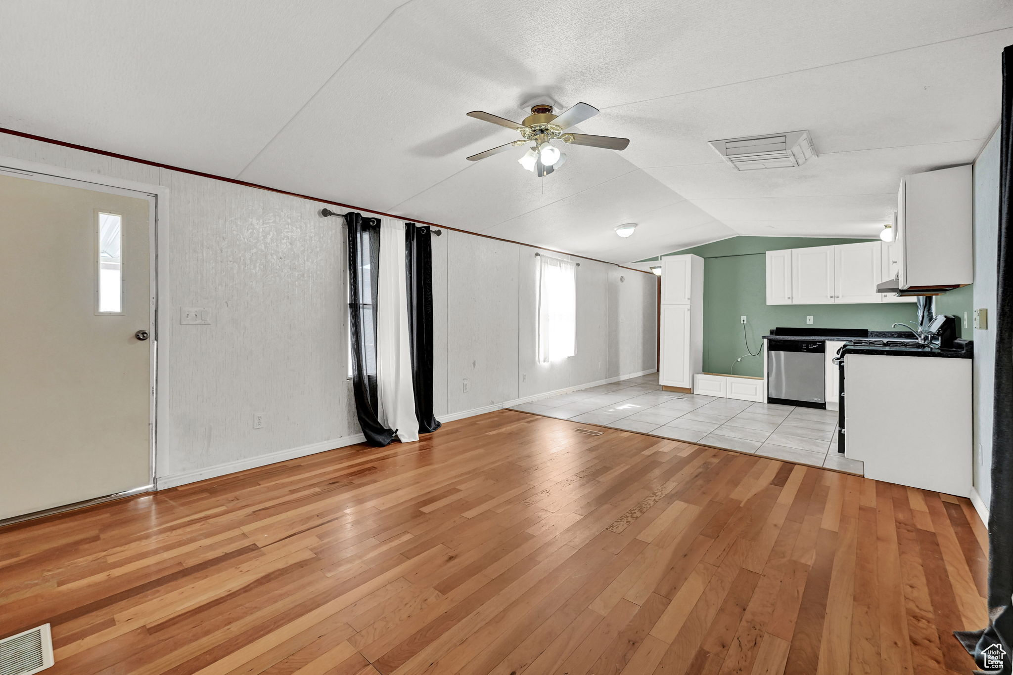 Unfurnished living room with light wood-type flooring, vaulted ceiling, a wealth of natural light, and ceiling fan