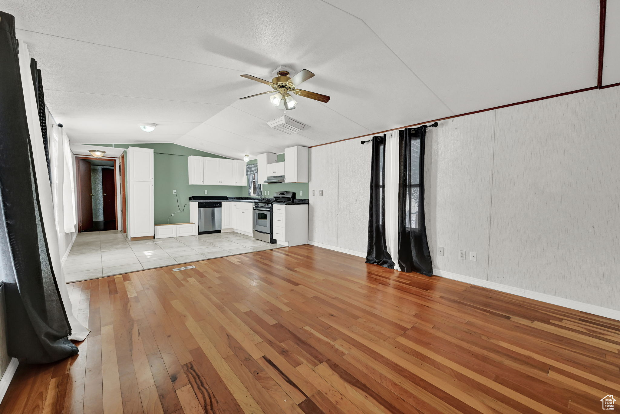 Unfurnished living room featuring ceiling fan, light wood-type flooring, sink, and vaulted ceiling