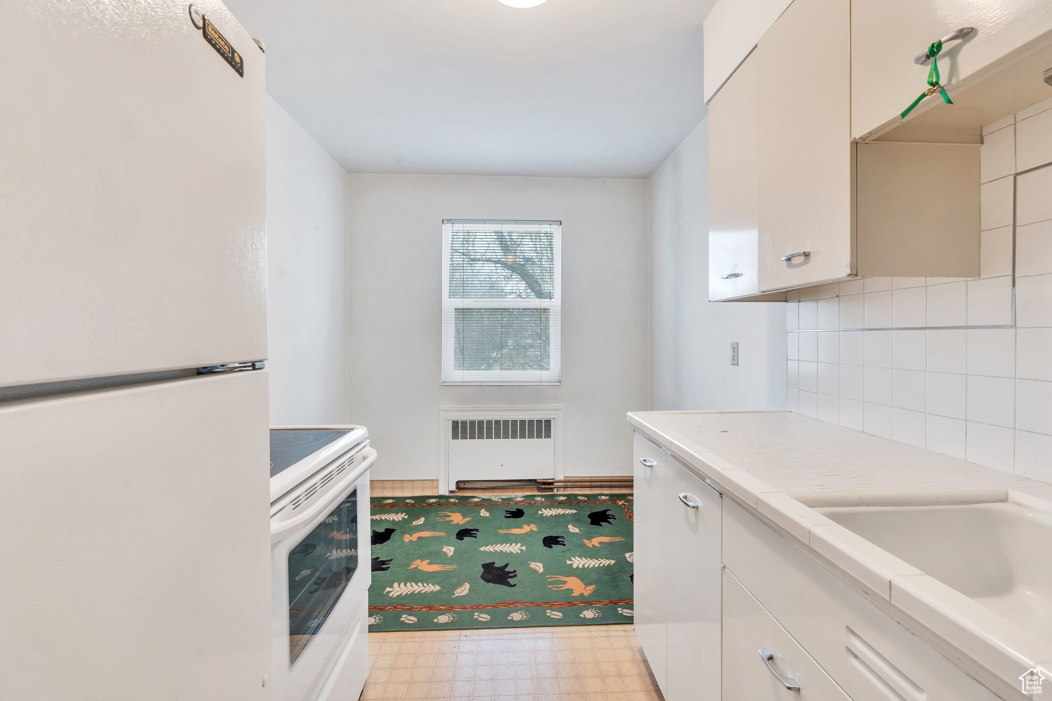 Kitchen featuring tasteful backsplash, radiator, white appliances, sink, and white cabinets