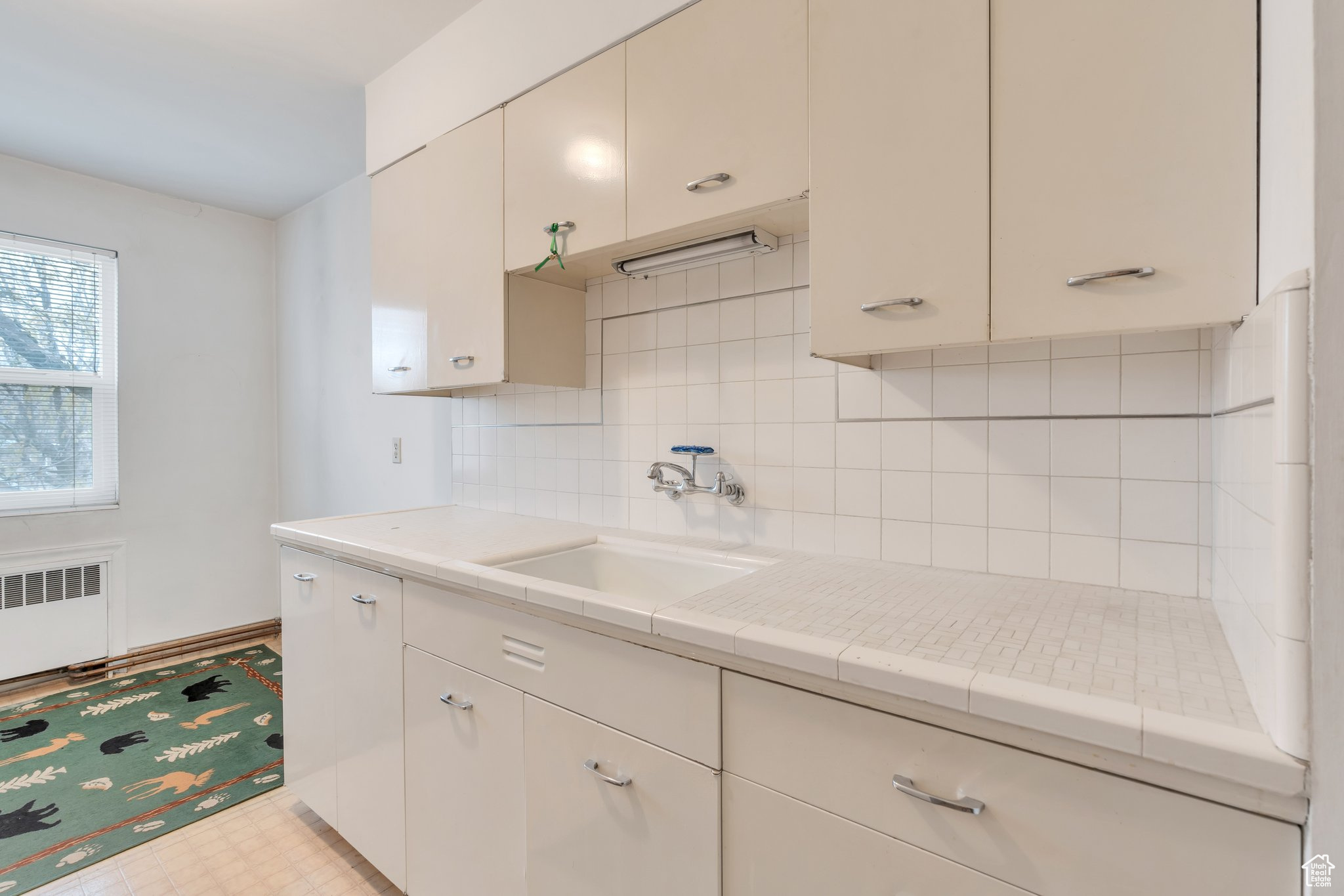 Kitchen with backsplash, light tile patterned flooring, sink, and radiator