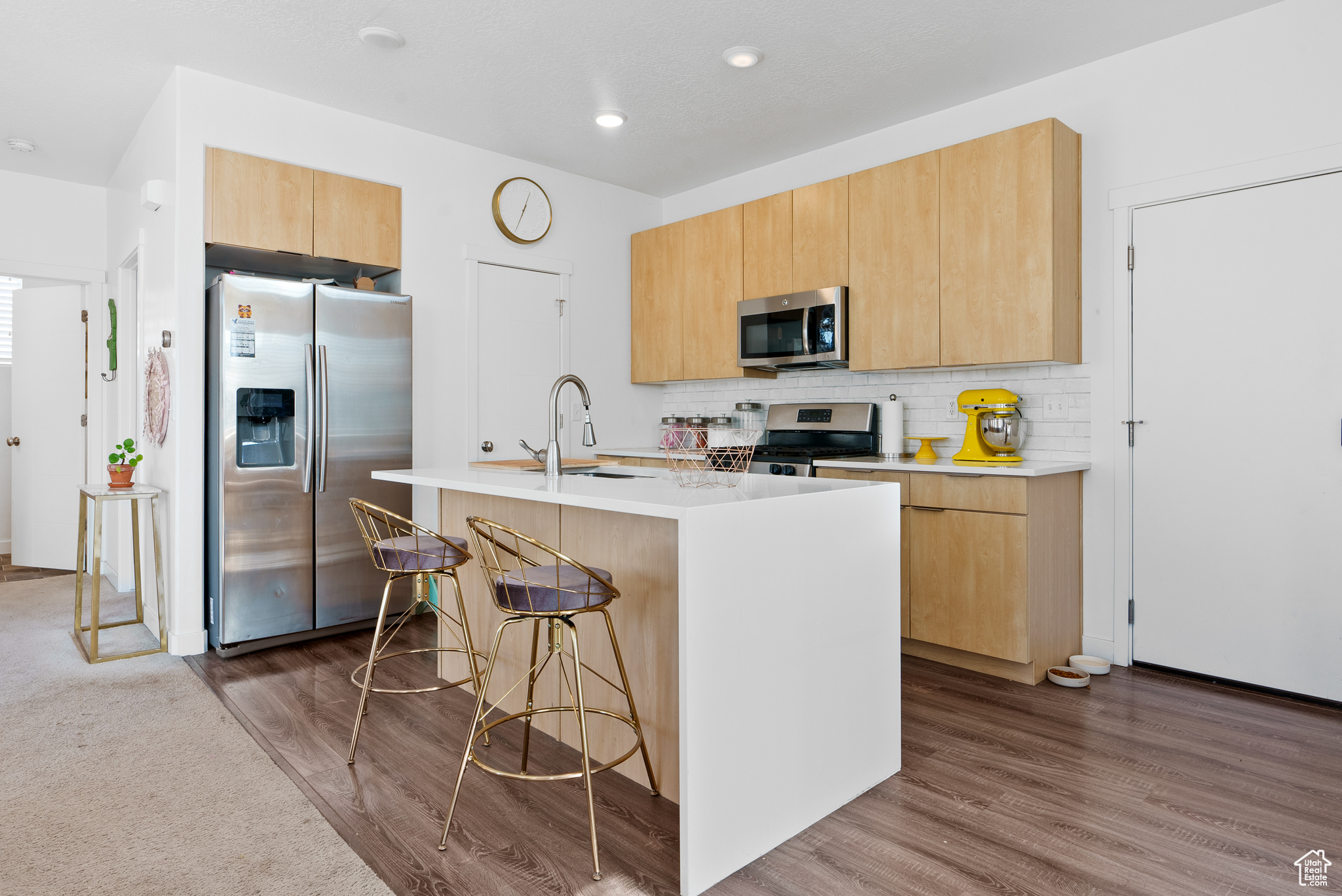 Kitchen with appliances with stainless steel finishes, dark hardwood / wood-style flooring, a center island with sink, and a breakfast bar area