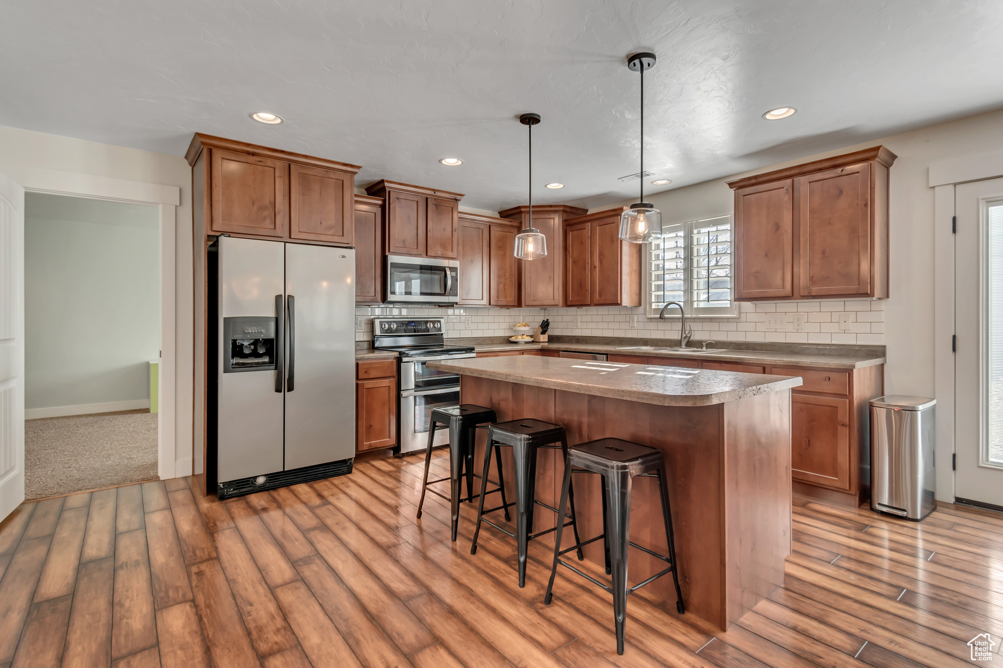 Kitchen featuring a center island, sink, stainless steel appliances, decorative light fixtures, and a breakfast bar area