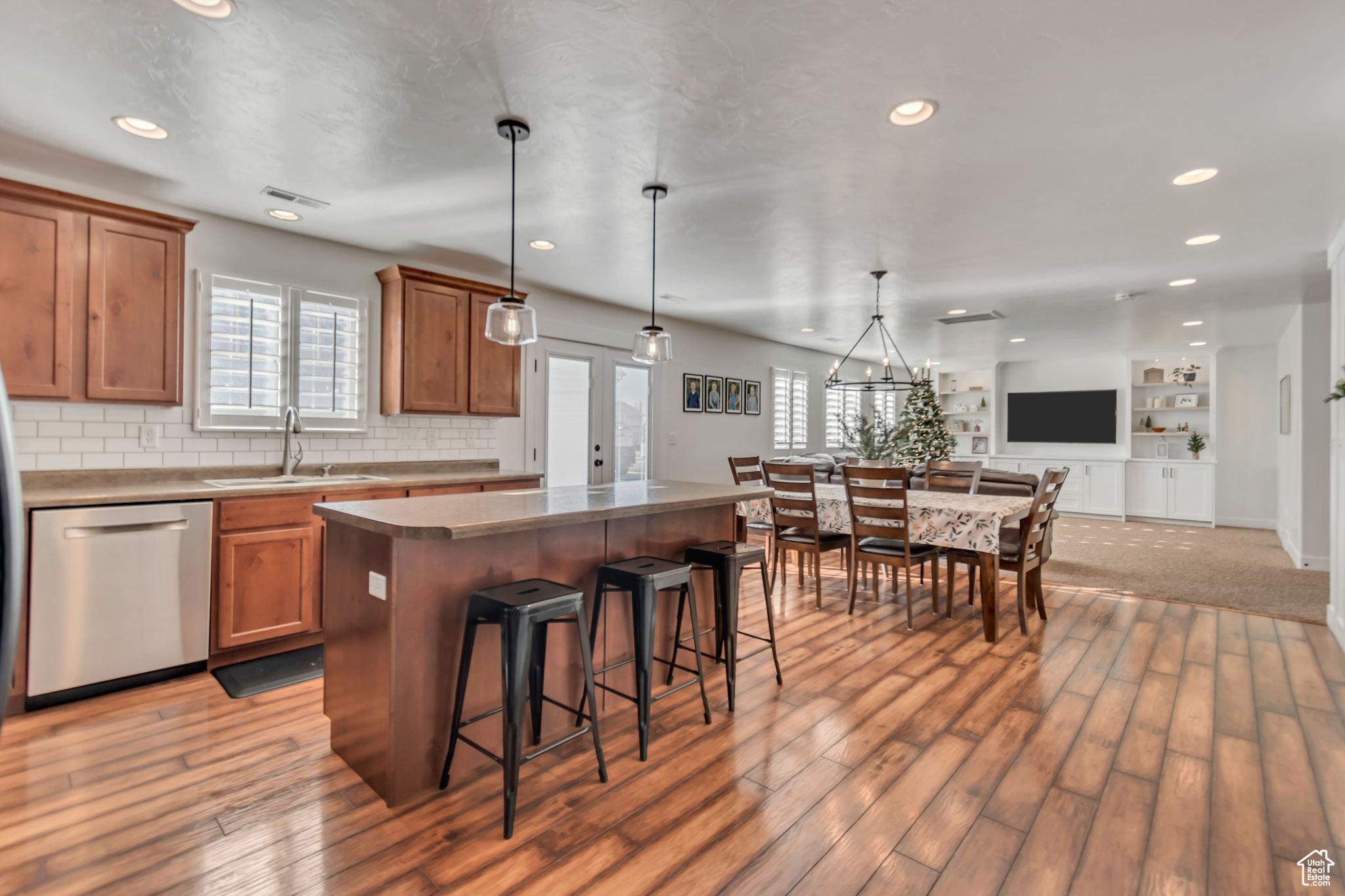 Kitchen featuring dishwasher, sink, light wood-type flooring, decorative light fixtures, and a kitchen island