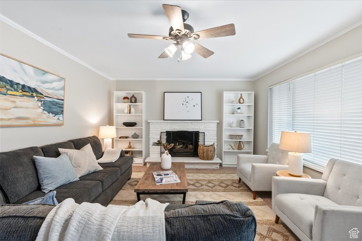 Living room with a stone fireplace, ceiling fan, and ornamental molding