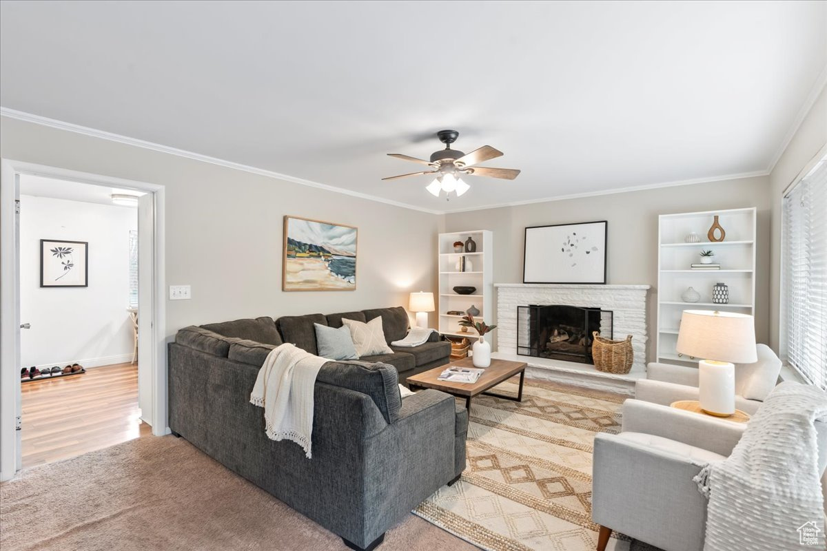 Living room featuring hardwood / wood-style flooring, a stone fireplace, ceiling fan, and ornamental molding