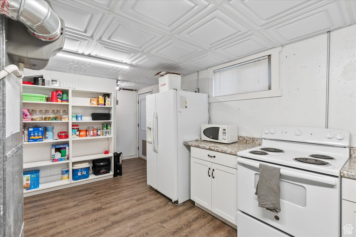 Kitchen with white appliances, hardwood / wood-style flooring, and white cabinetry