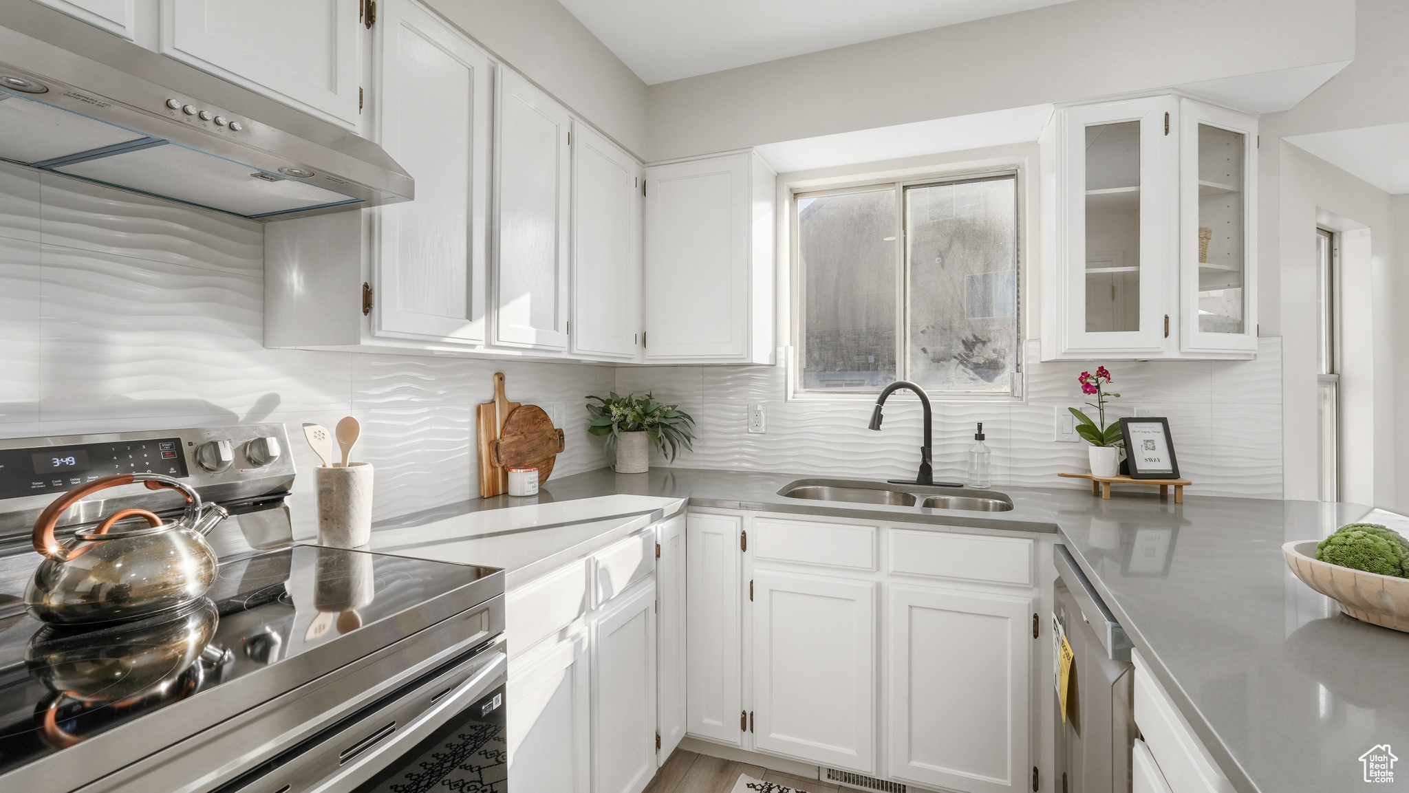 Kitchen with white cabinets, extractor fan, stainless steel electric stove, and sink