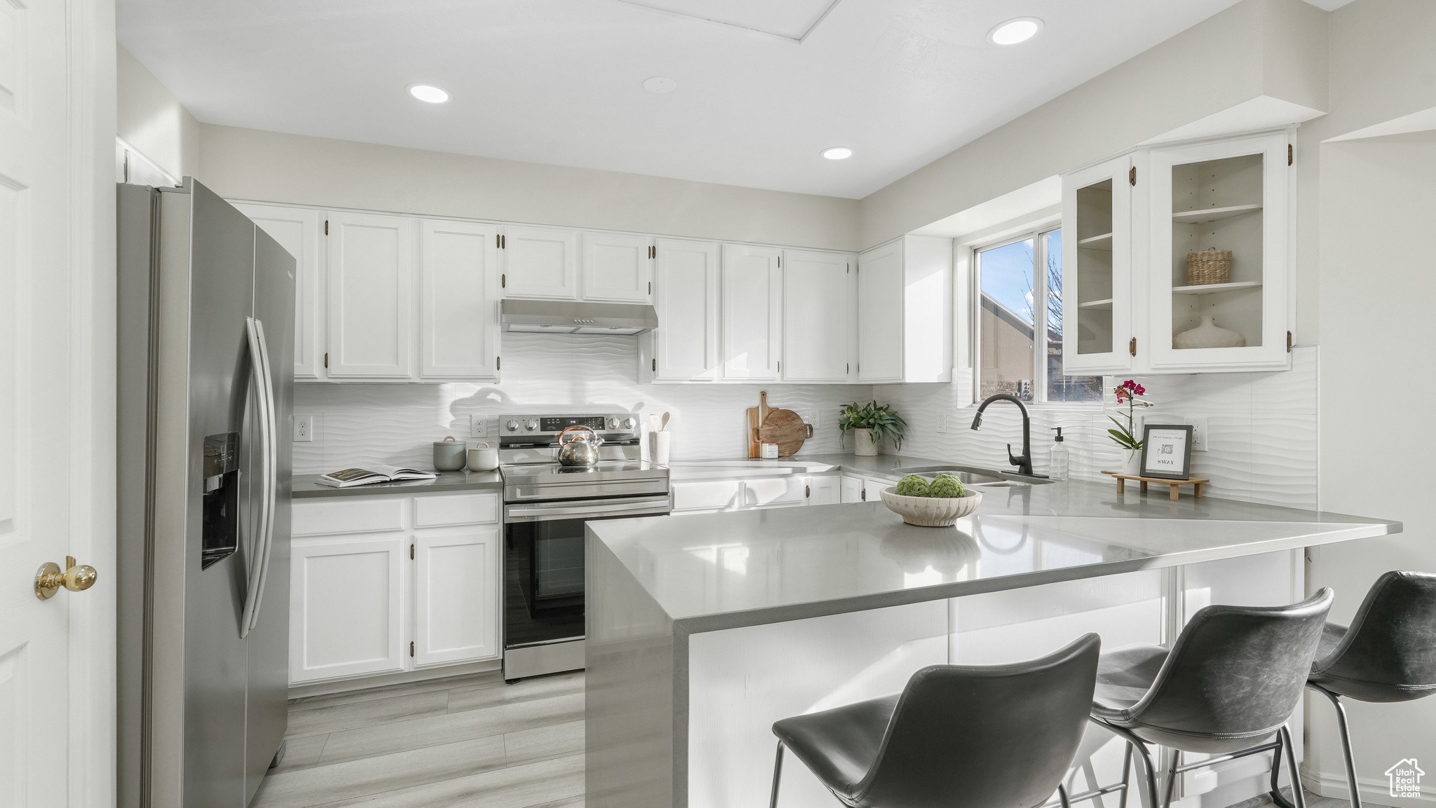 Kitchen with white cabinetry, sink, stainless steel appliances, backsplash, and a breakfast bar area