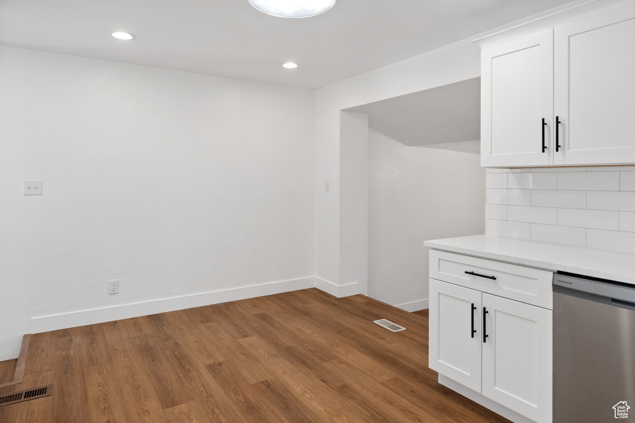 Kitchen with decorative backsplash, light hardwood / wood-style flooring, white cabinets, and stainless steel dishwasher