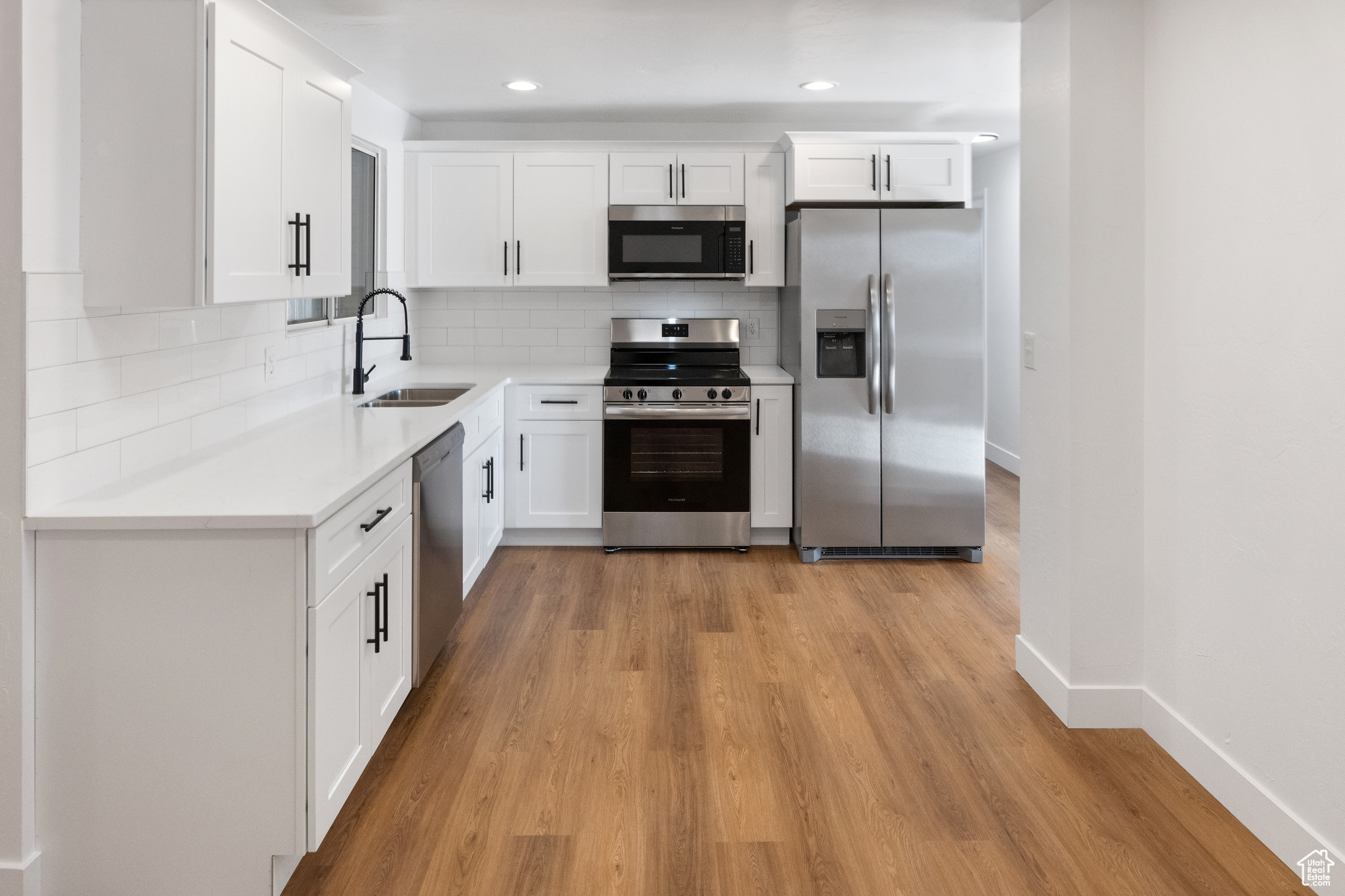 Kitchen with sink, decorative backsplash, appliances with stainless steel finishes, light hardwood / wood-style floors, and white cabinetry