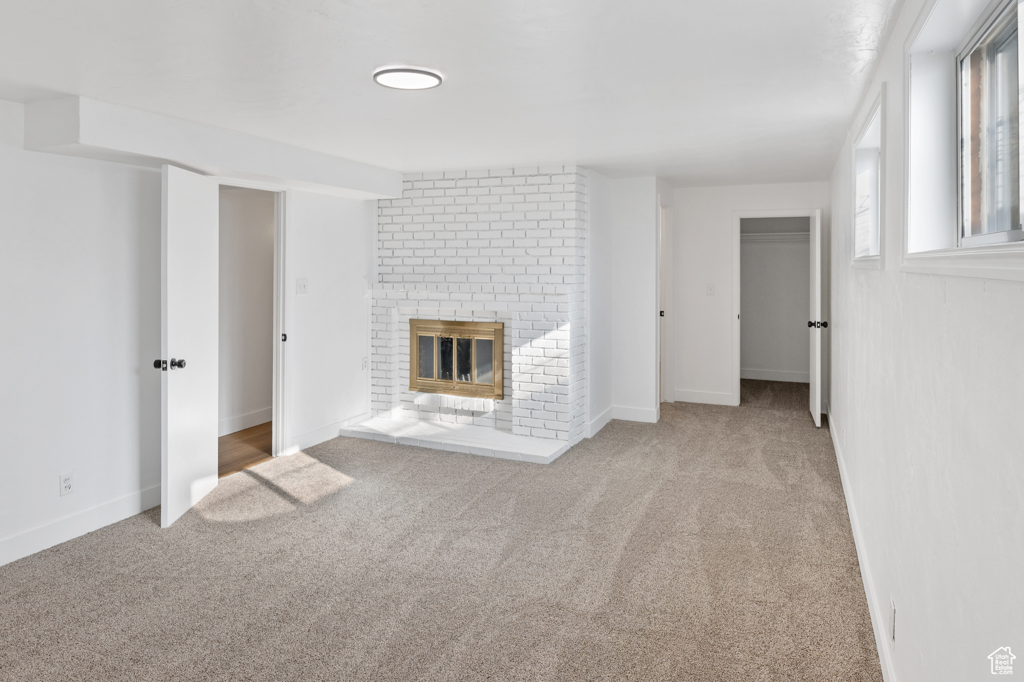 Unfurnished living room featuring light colored carpet and a brick fireplace