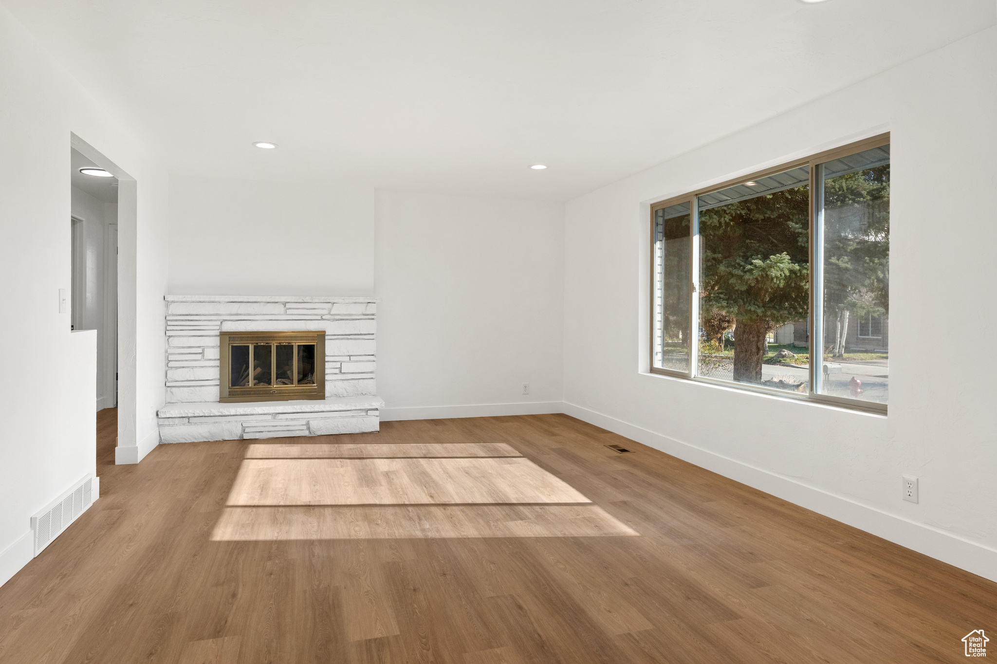 Unfurnished living room with a stone fireplace and wood-type flooring