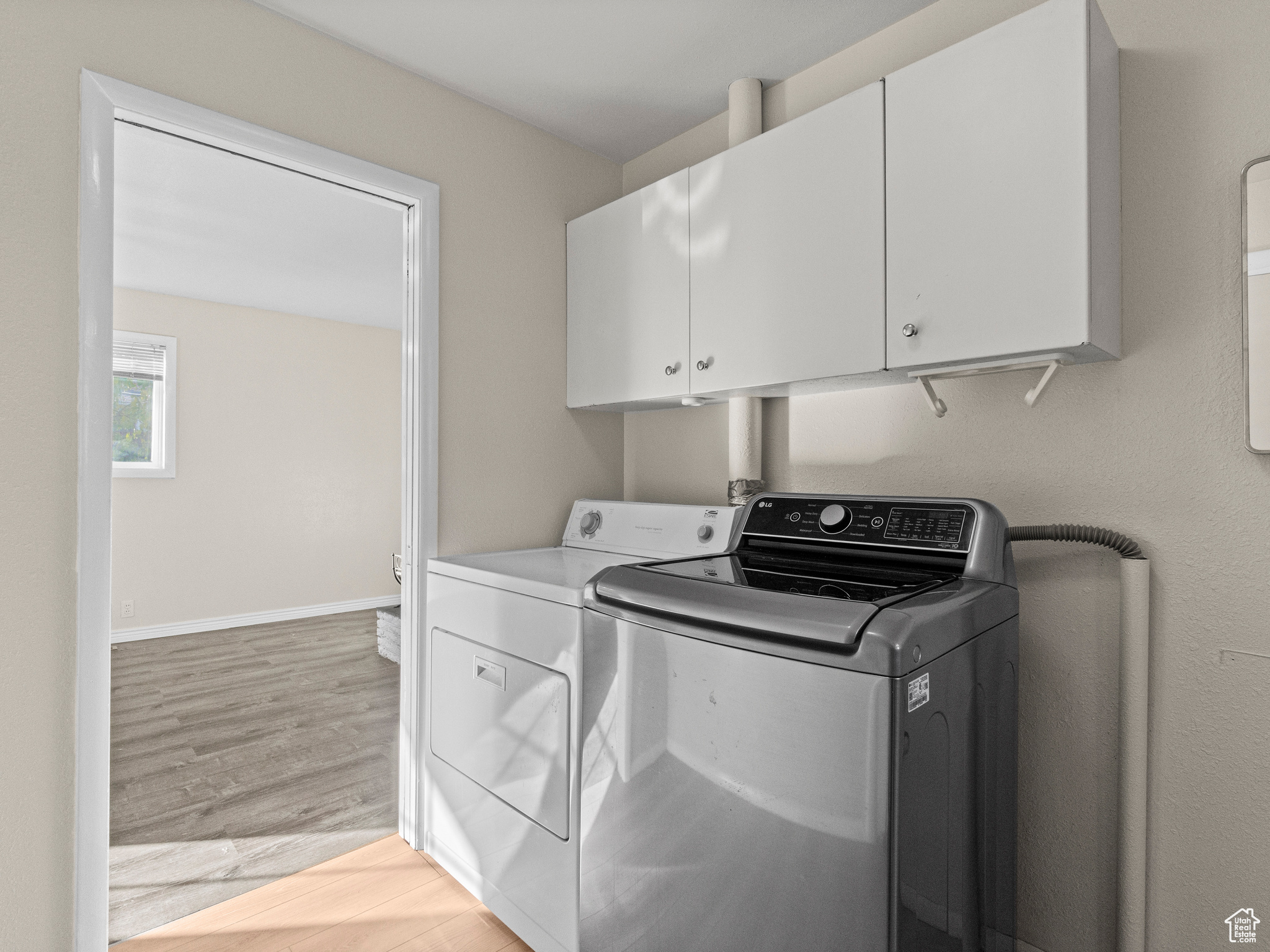 Washroom featuring washing machine and clothes dryer, light hardwood / wood-style flooring, and cabinets