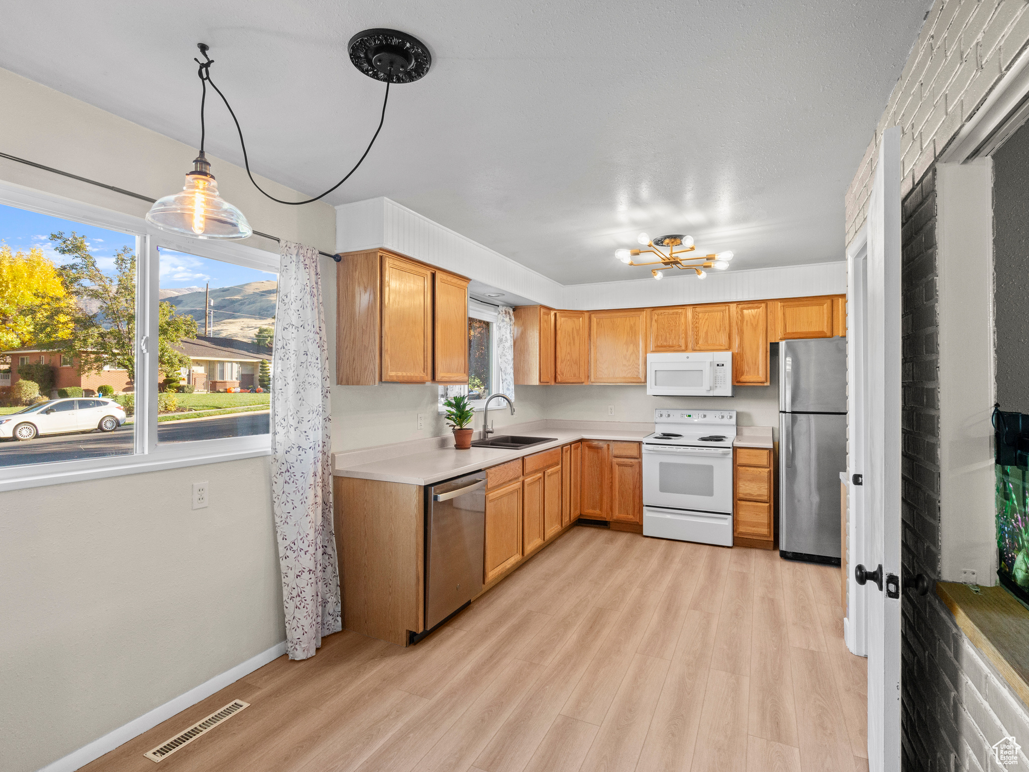 Kitchen with appliances with stainless steel finishes, sink, a notable chandelier, light hardwood / wood-style floors, and hanging light fixtures