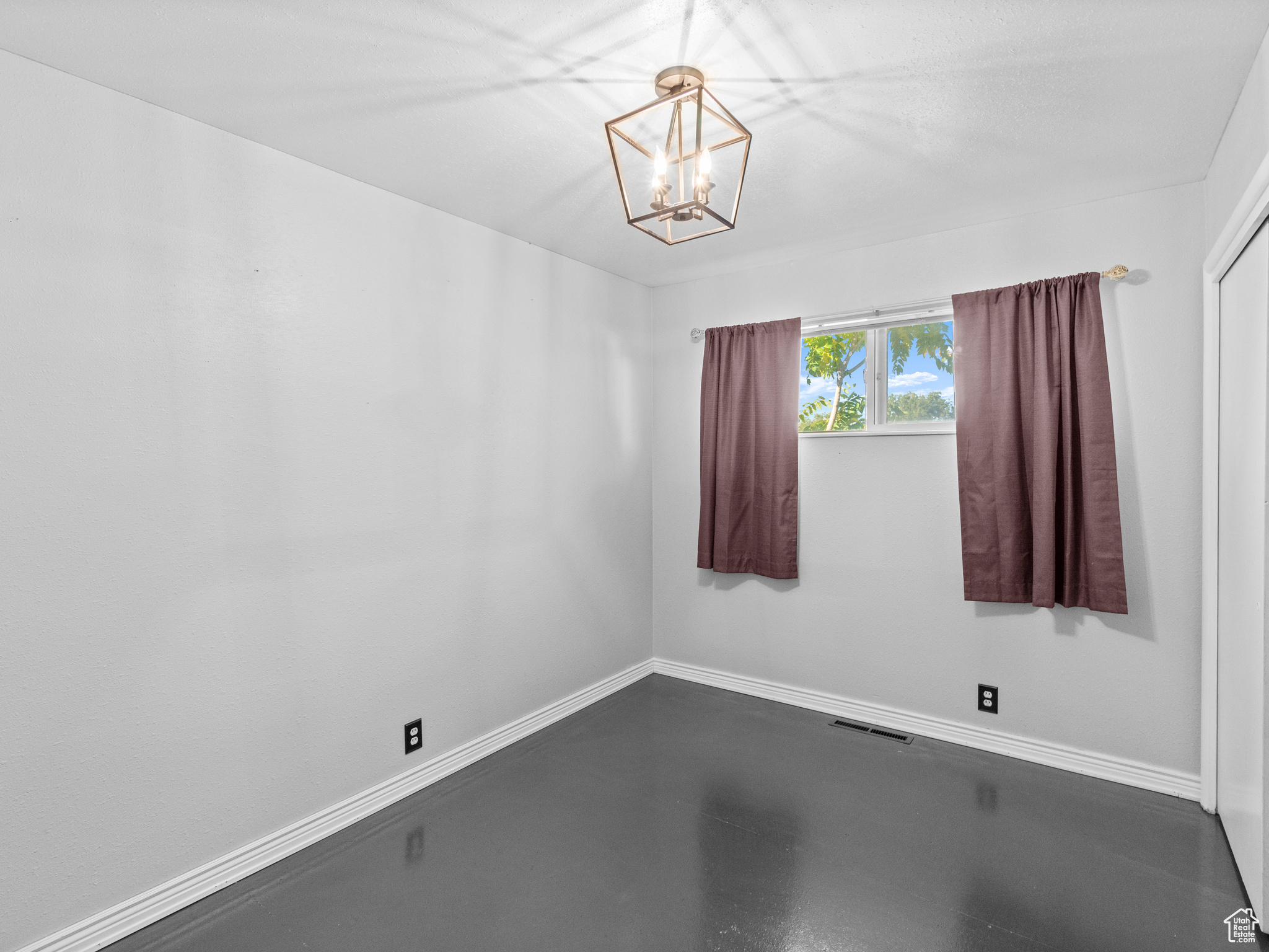 Empty room featuring concrete floors and an inviting chandelier