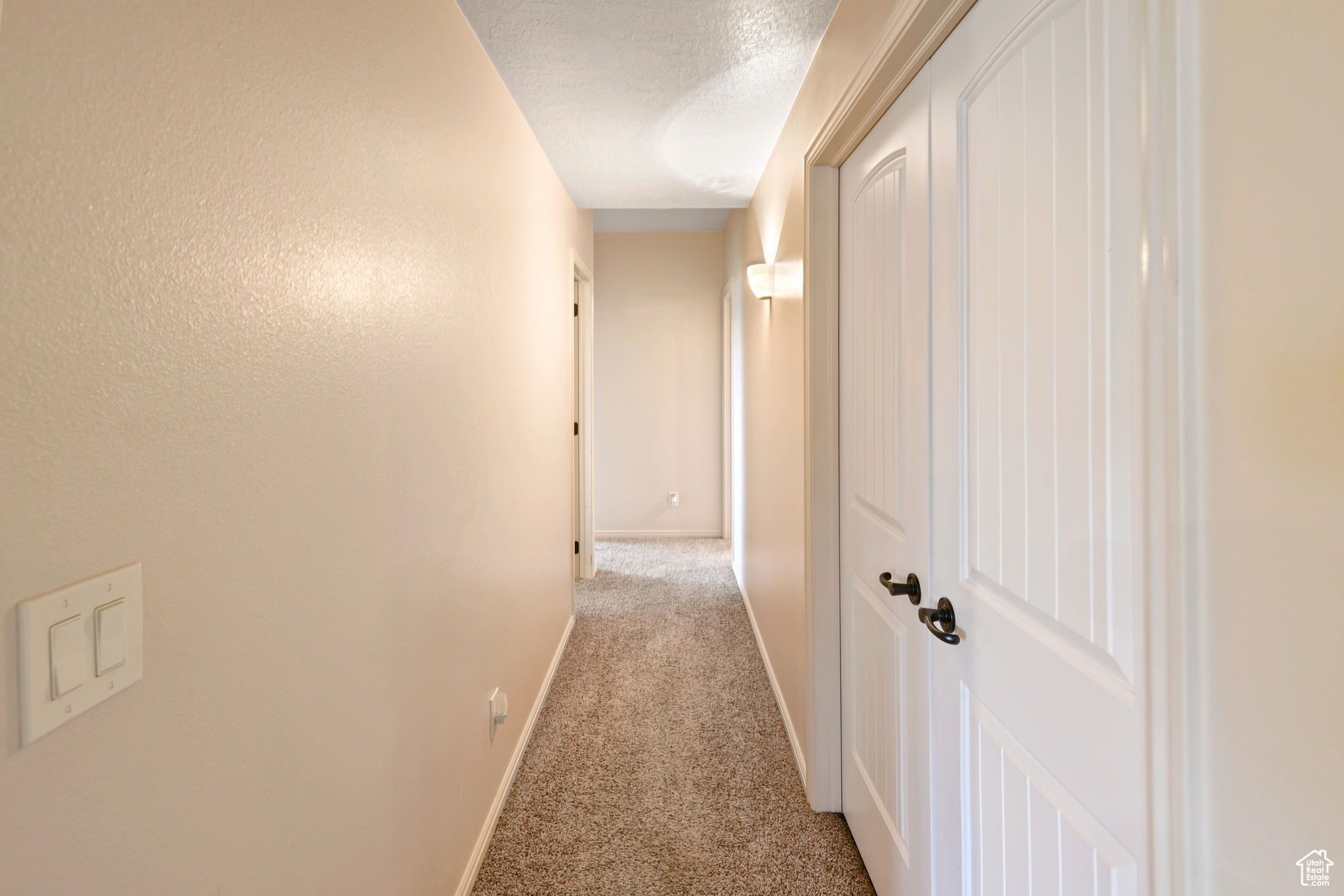 Hall featuring a textured ceiling and light colored carpet