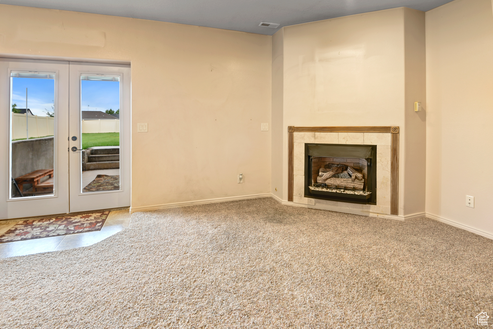 Unfurnished living room with carpet flooring, a tile fireplace, and french doors