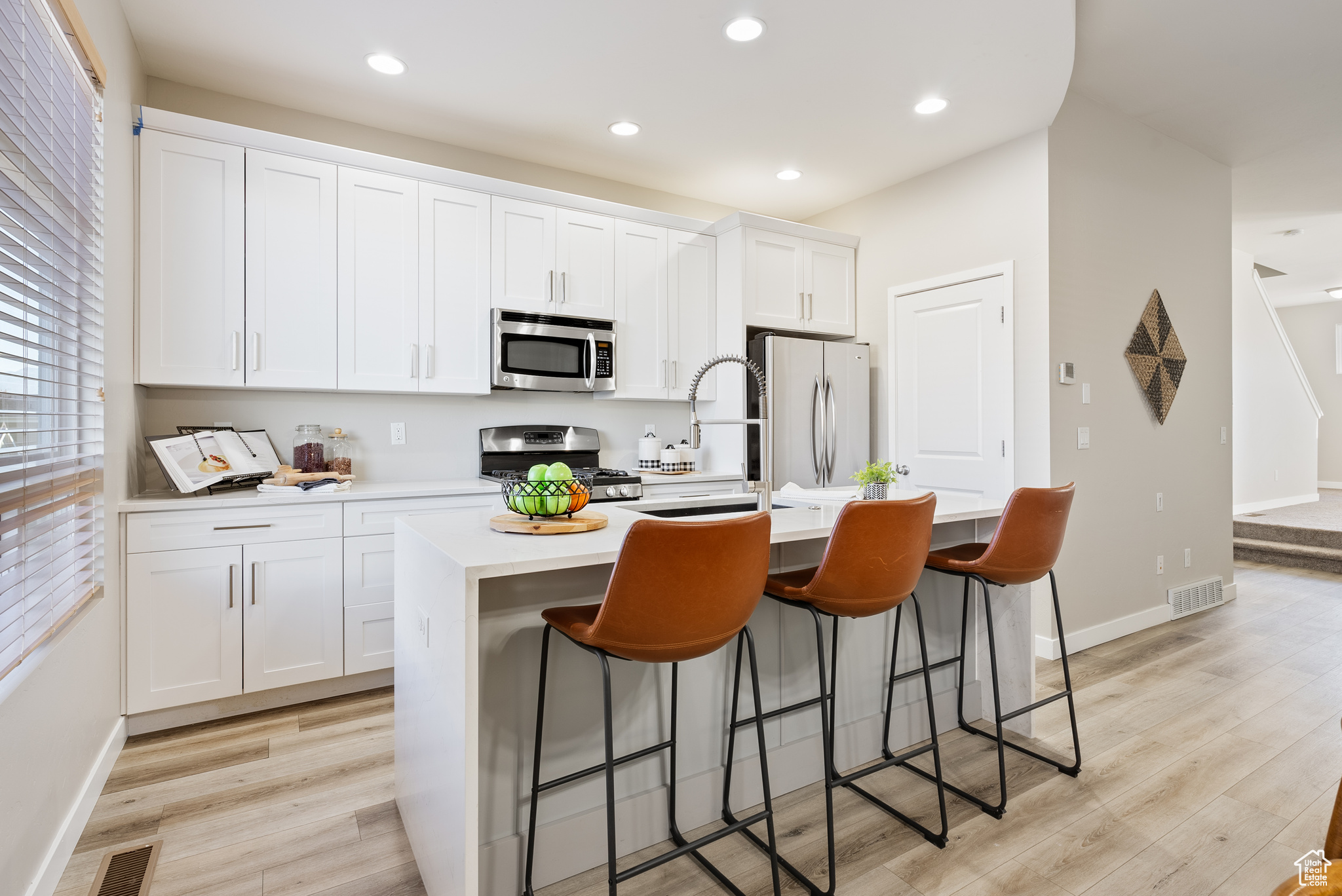 Kitchen with a kitchen island with sink, light wood-type flooring, appliances with stainless steel finishes, a kitchen bar, and white cabinetry