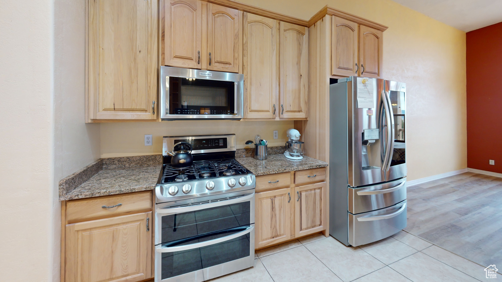 Kitchen with light wood-type flooring, light stone countertops, stainless steel appliances, and light brown cabinetry