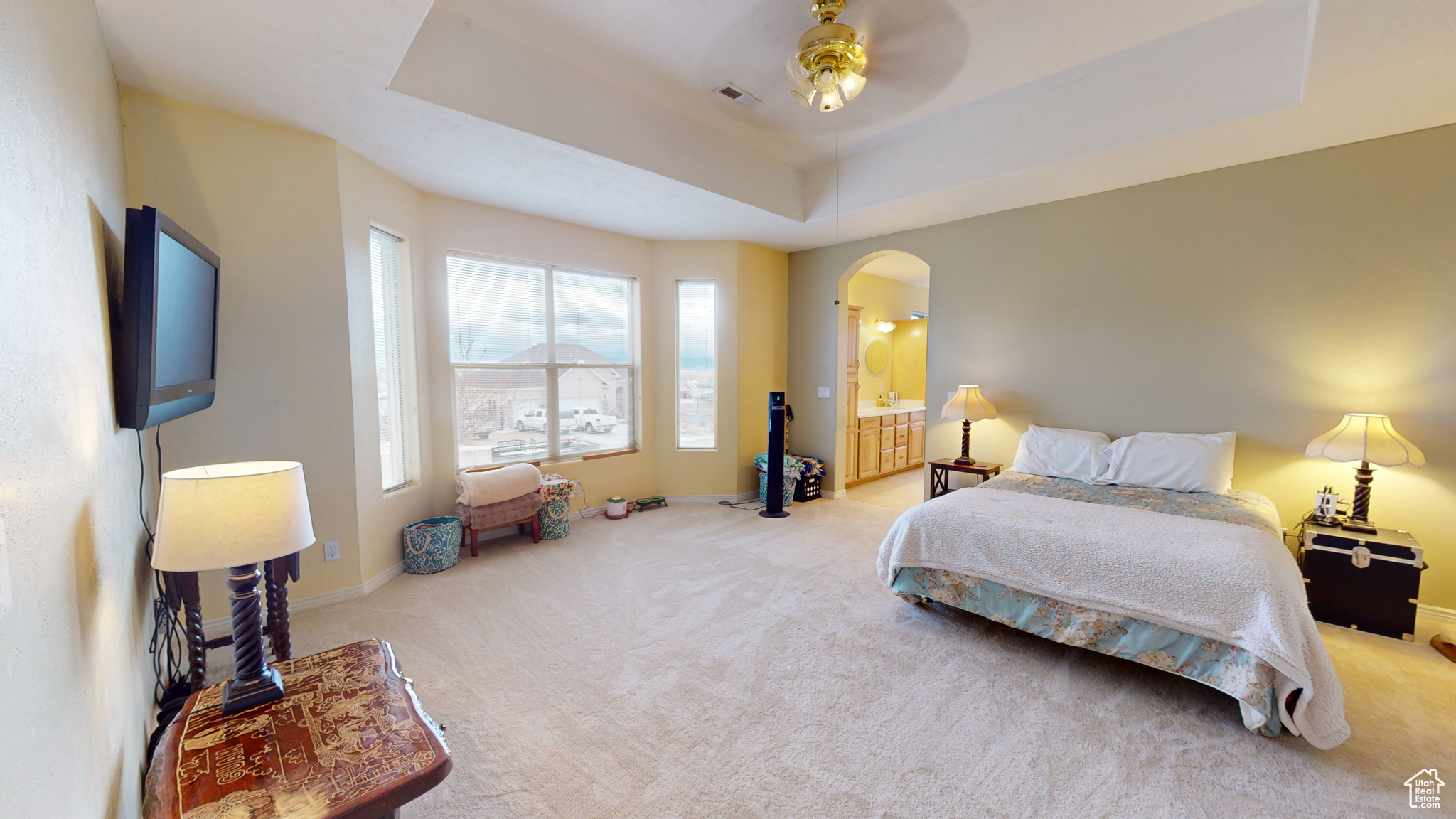 Bedroom featuring ceiling fan, light carpet, connected bathroom, and a tray ceiling