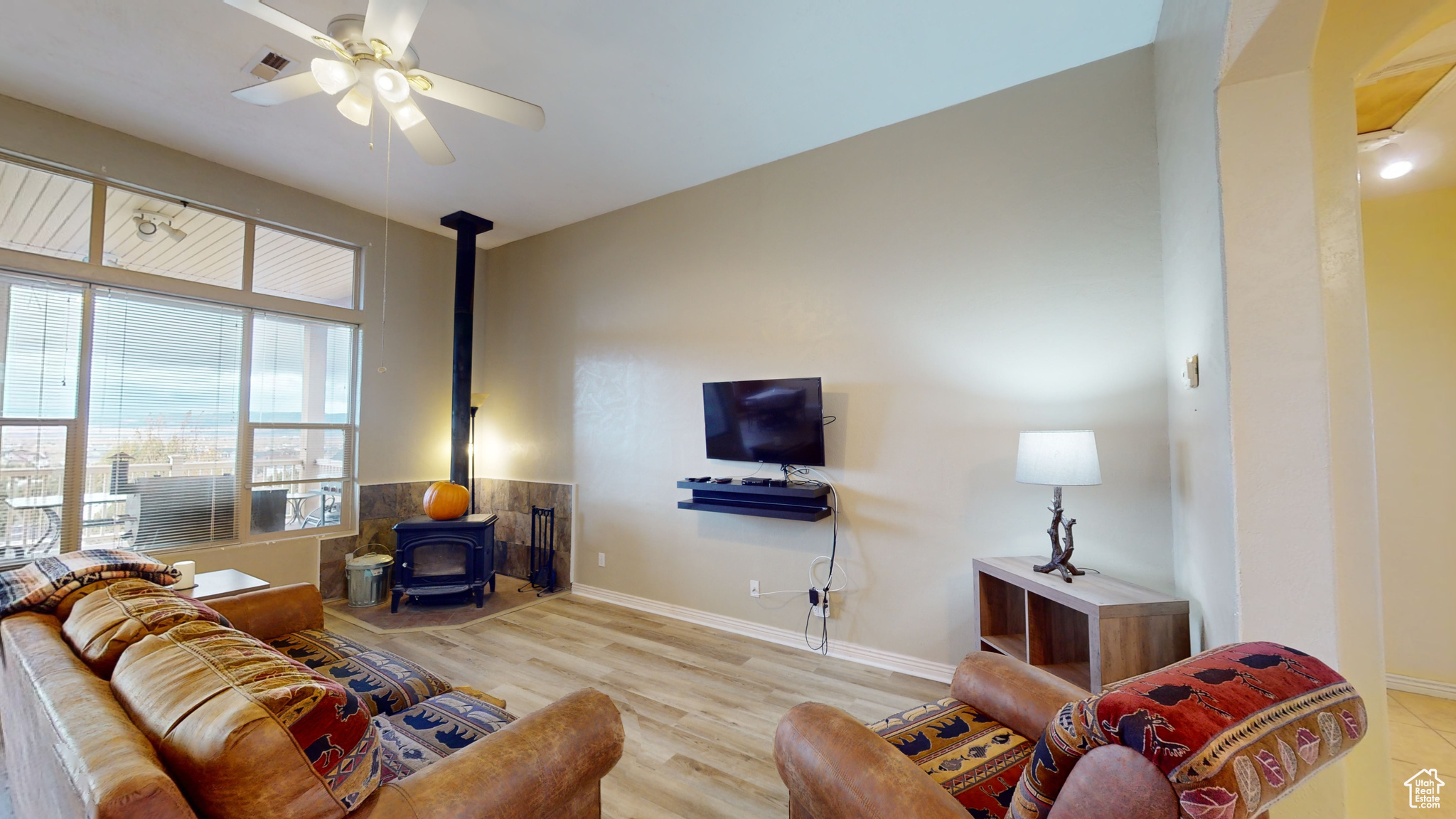 Living room with ceiling fan, a wood stove, and light hardwood / wood-style flooring