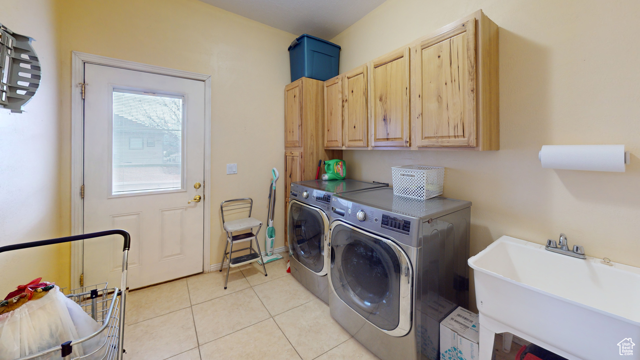 Clothes washing area featuring cabinets, light tile patterned floors, washing machine and dryer, and sink