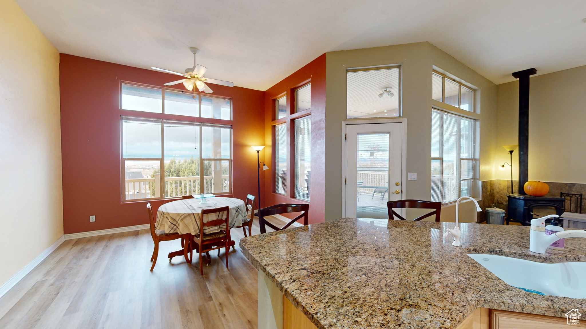 Kitchen featuring light wood-type flooring, light stone counters, ceiling fan, sink, and a wood stove