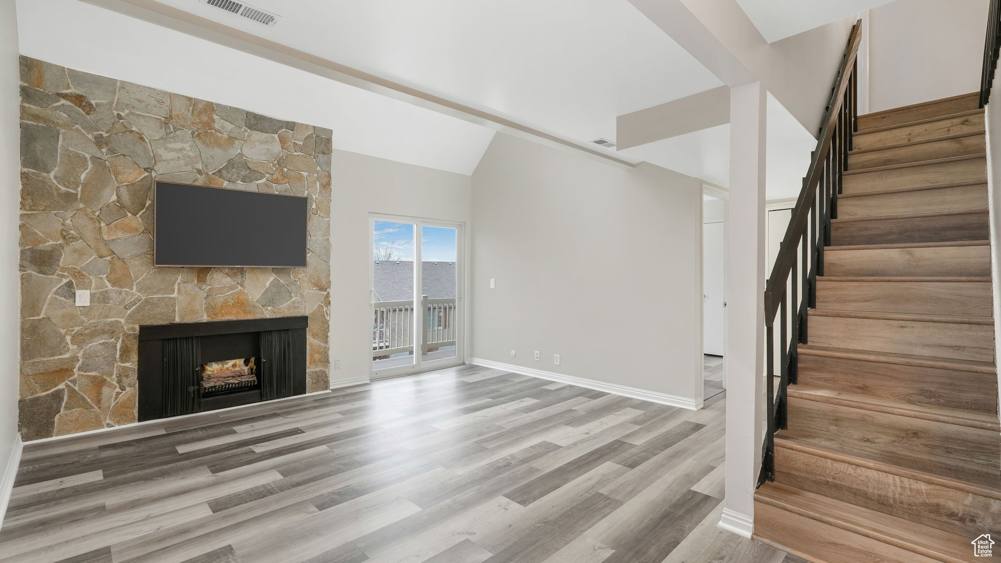 Unfurnished living room with hardwood / wood-style flooring, a stone fireplace, and lofted ceiling