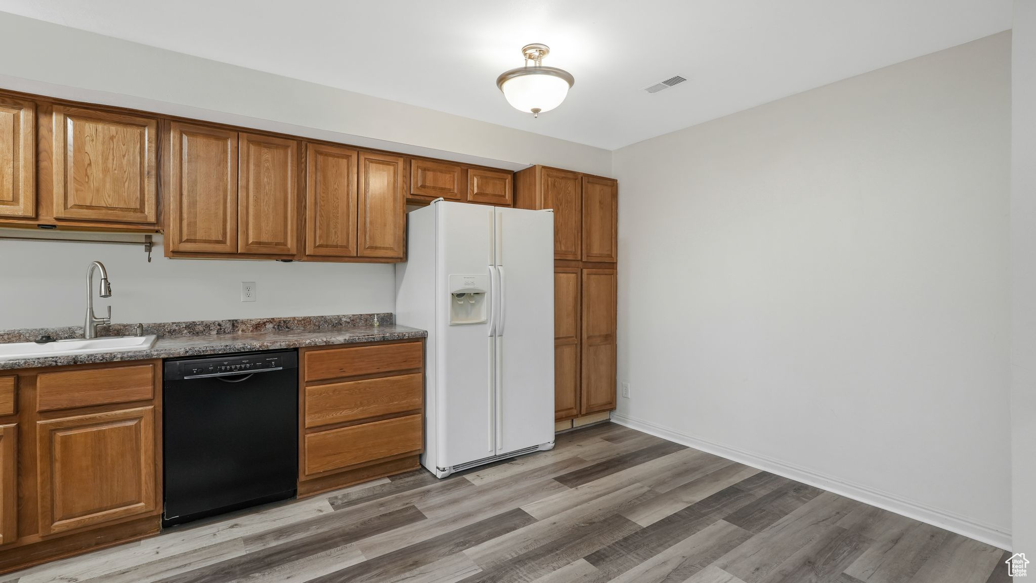 Kitchen with sink, black dishwasher, white refrigerator with ice dispenser, dark stone countertops, and light hardwood / wood-style floors