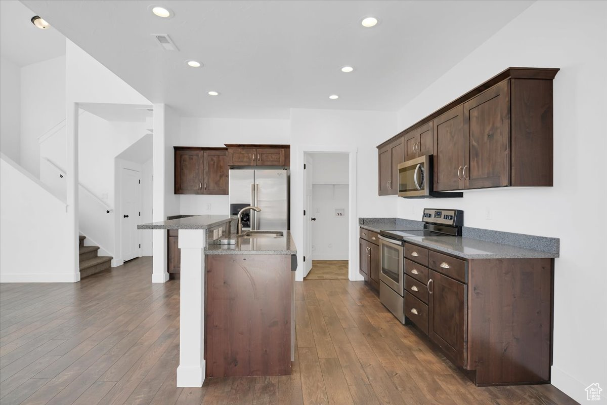 Kitchen with dark brown cabinetry, a kitchen island with sink, appliances with stainless steel finishes, and dark wood-type flooring