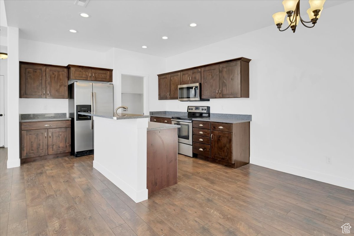 Kitchen featuring decorative light fixtures, stainless steel appliances, dark hardwood / wood-style floors, and a center island with sink