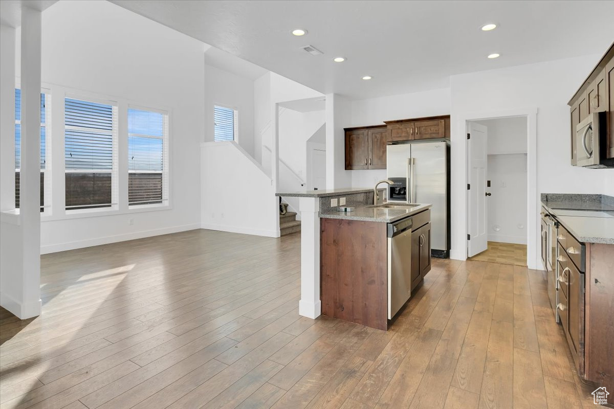 Kitchen featuring light stone countertops, a center island with sink, stainless steel appliances, and light wood-type flooring