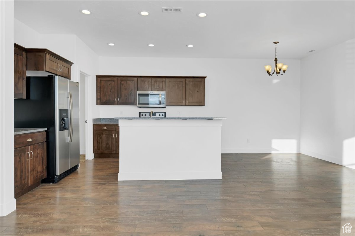 Kitchen with dark brown cabinetry, hanging light fixtures, wood-type flooring, and appliances with stainless steel finishes