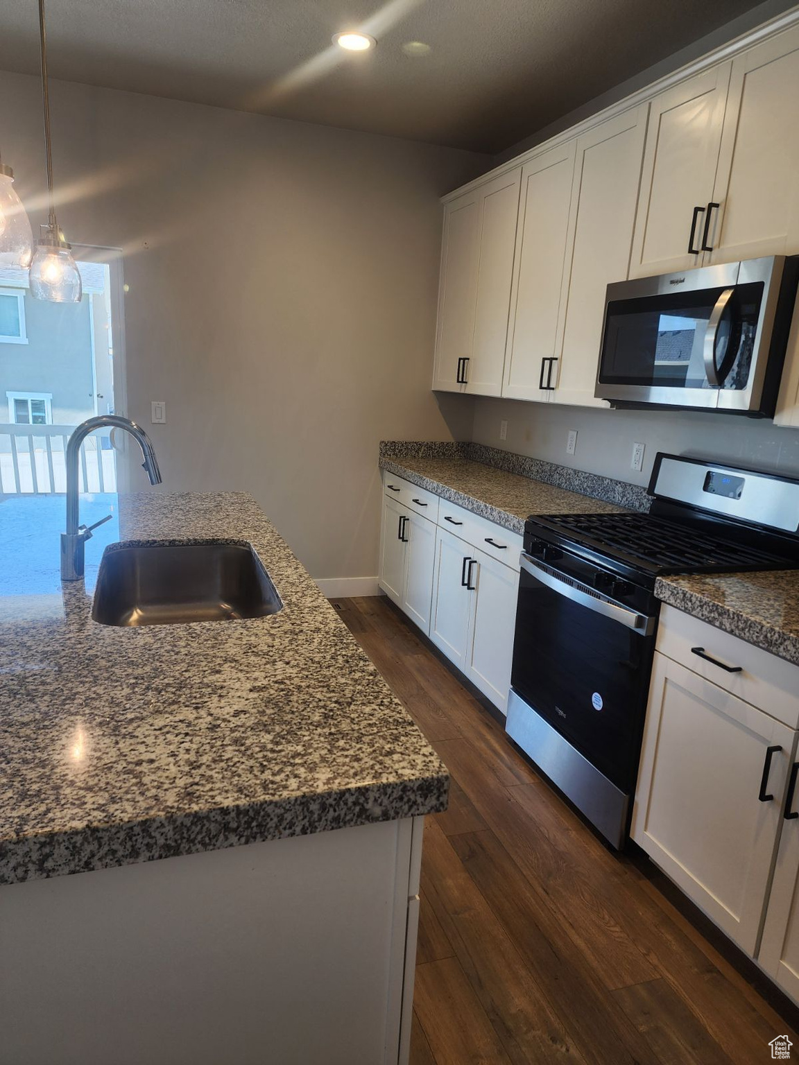 Kitchen with white cabinetry, sink, hanging light fixtures, dark wood-type flooring, and appliances with stainless steel finishes