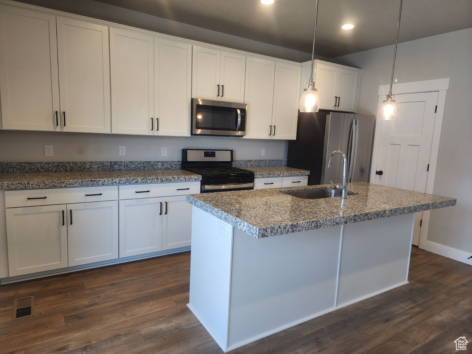 Kitchen with sink, white cabinets, stainless steel appliances, and decorative light fixtures