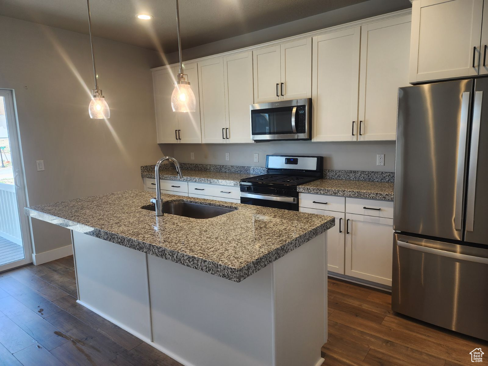 Kitchen with pendant lighting, sink, dark hardwood / wood-style flooring, white cabinetry, and stainless steel appliances