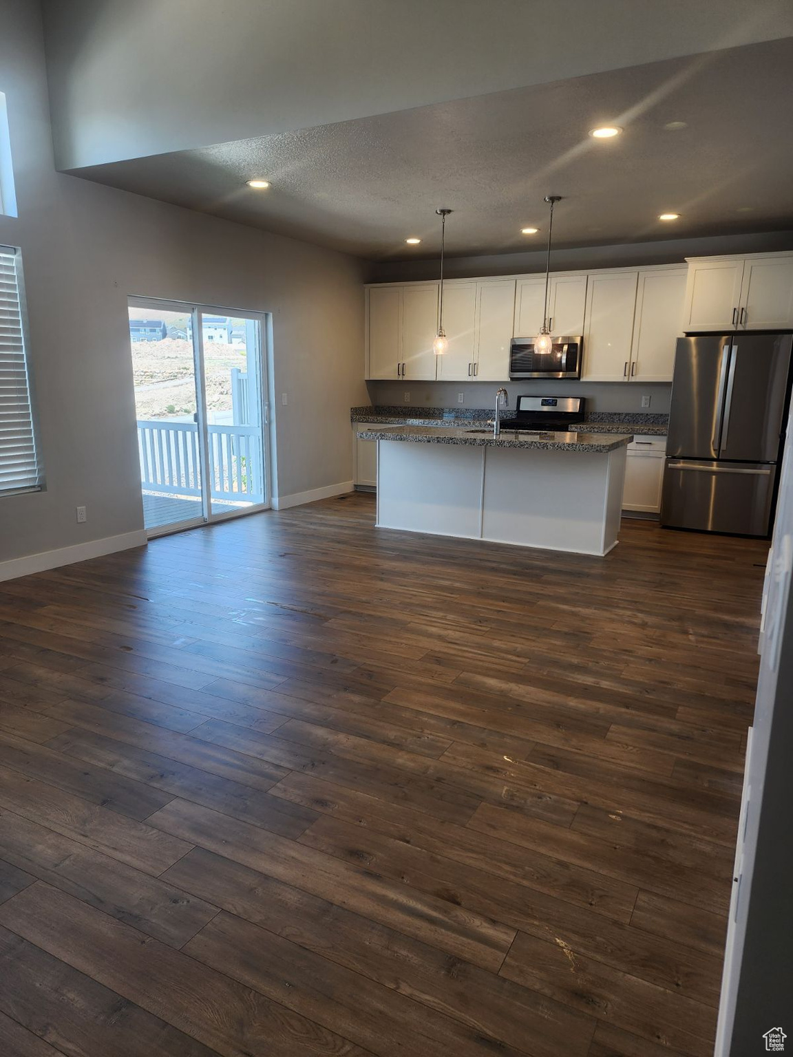 Kitchen with a center island with sink, dark wood-type flooring, decorative light fixtures, and appliances with stainless steel finishes