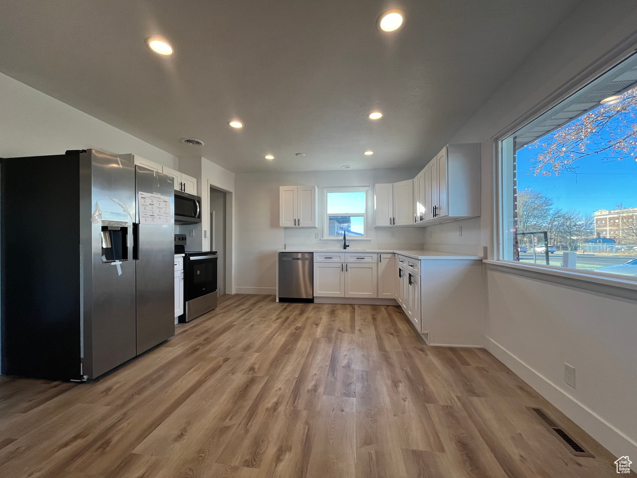 Kitchen with white cabinetry, sink, light hardwood / wood-style floors, and appliances with stainless steel finishes