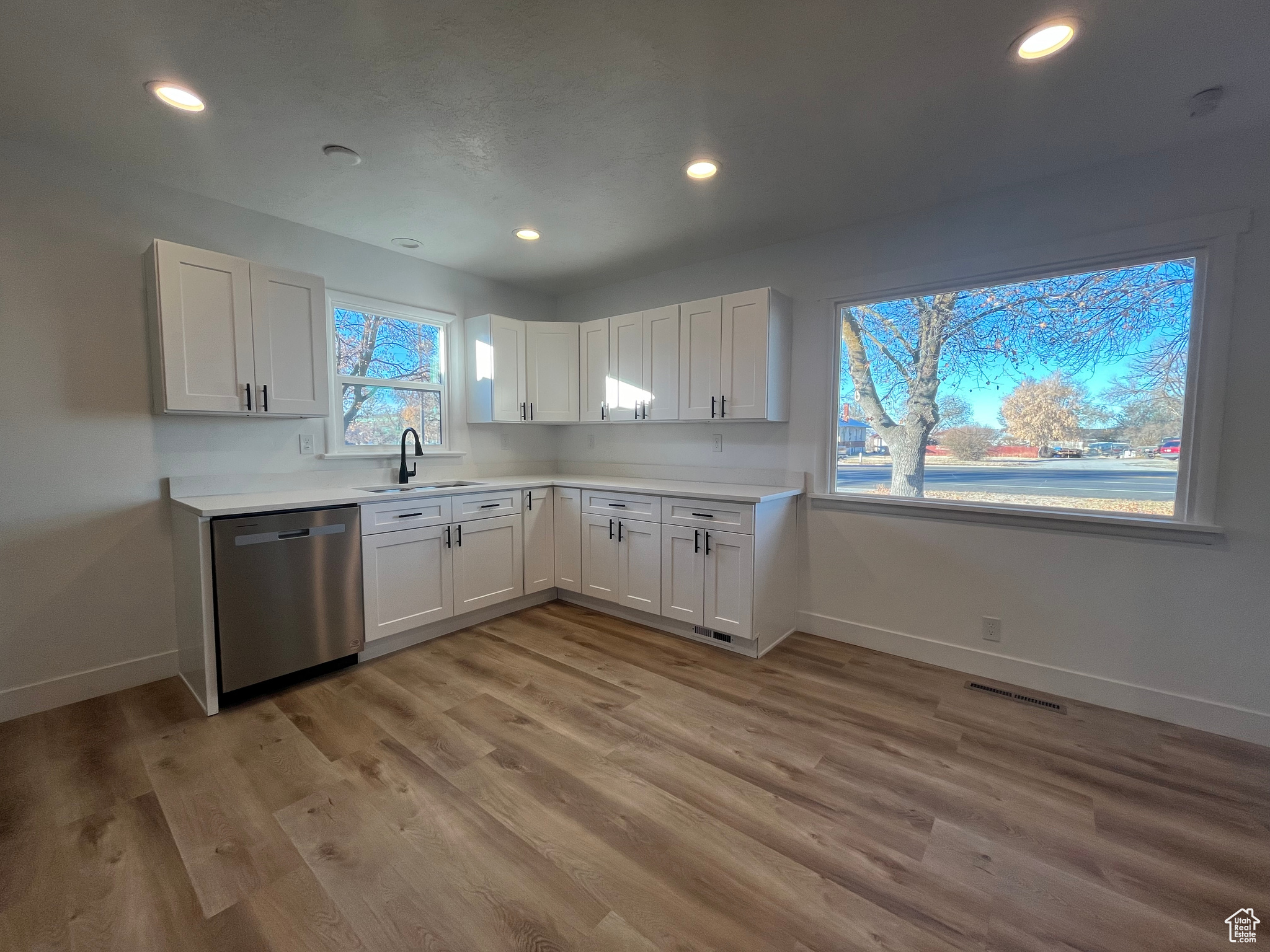 Kitchen with dishwasher, light hardwood / wood-style flooring, white cabinetry, and sink