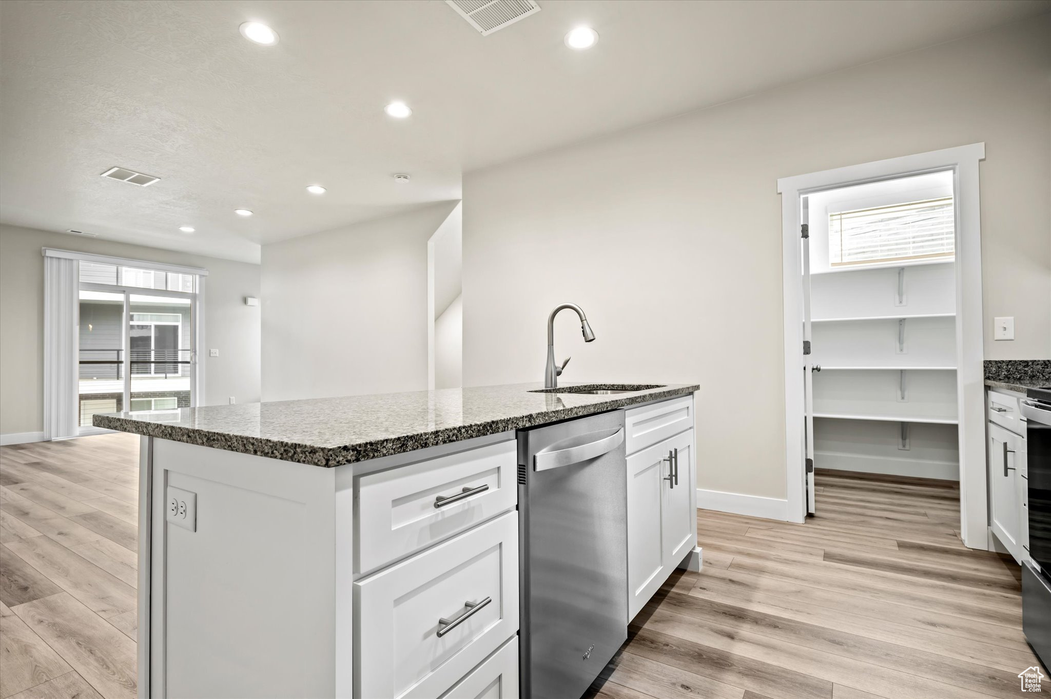 Kitchen with an island with sink, stainless steel dishwasher, light hardwood / wood-style floors, and sink