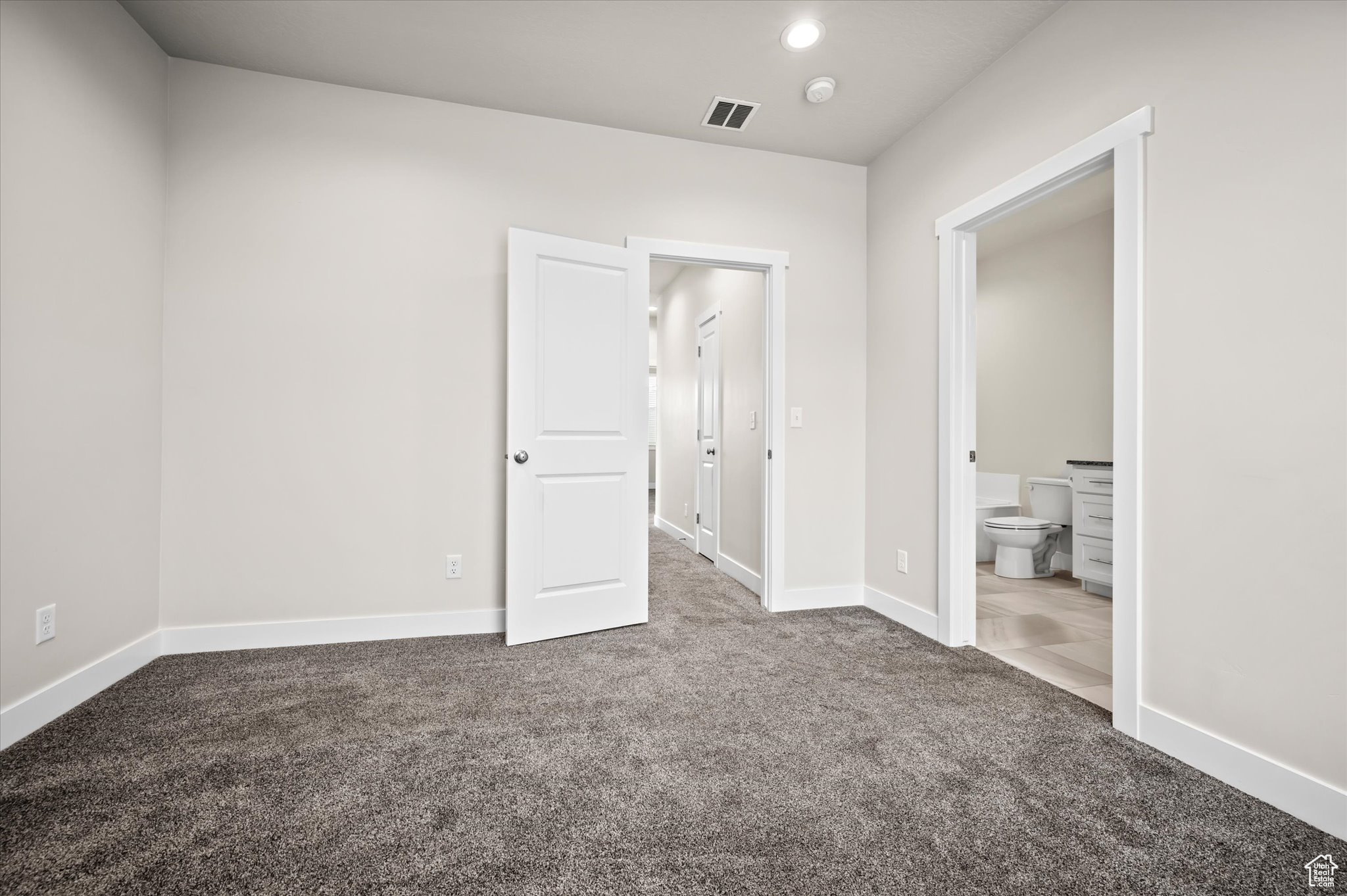 Unfurnished bedroom with dark colored carpet and ensuite bathroom