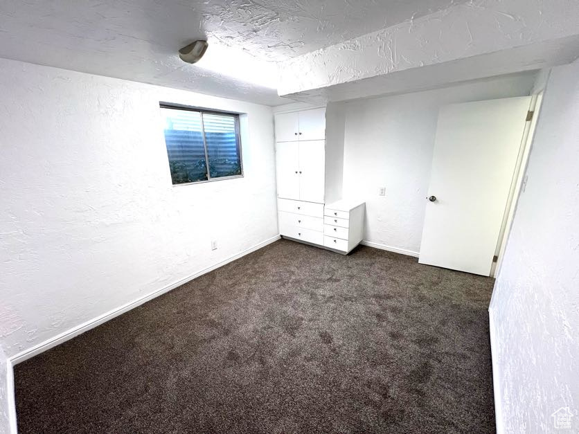 Unfurnished bedroom with dark carpet and a textured ceiling