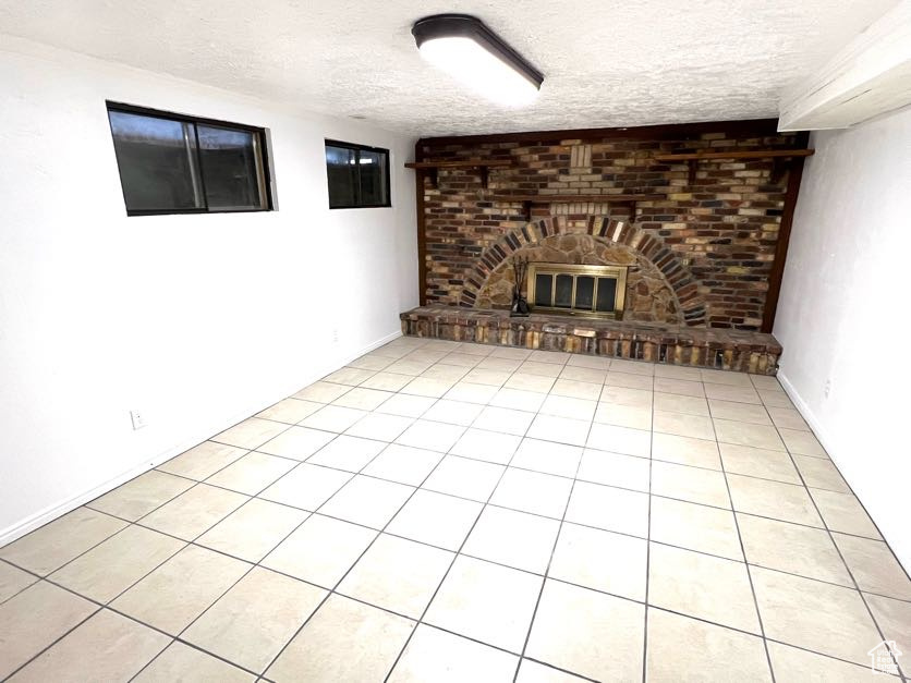 Unfurnished living room featuring a fireplace, light tile patterned flooring, and a textured ceiling