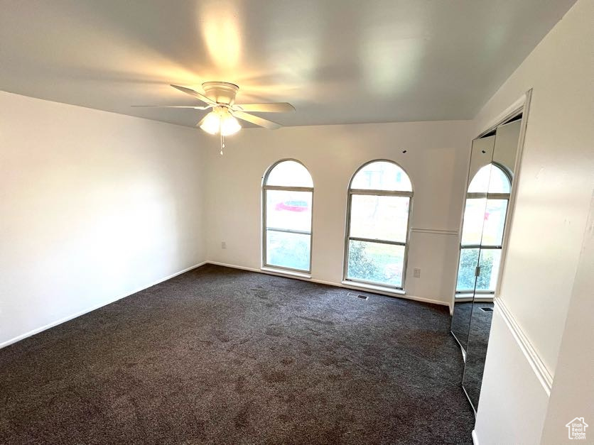 Unfurnished room featuring dark colored carpet and ceiling fan