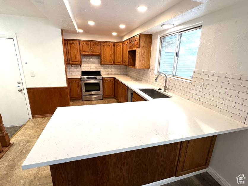 Kitchen with light wood-type flooring, kitchen peninsula, sink, and stainless steel range