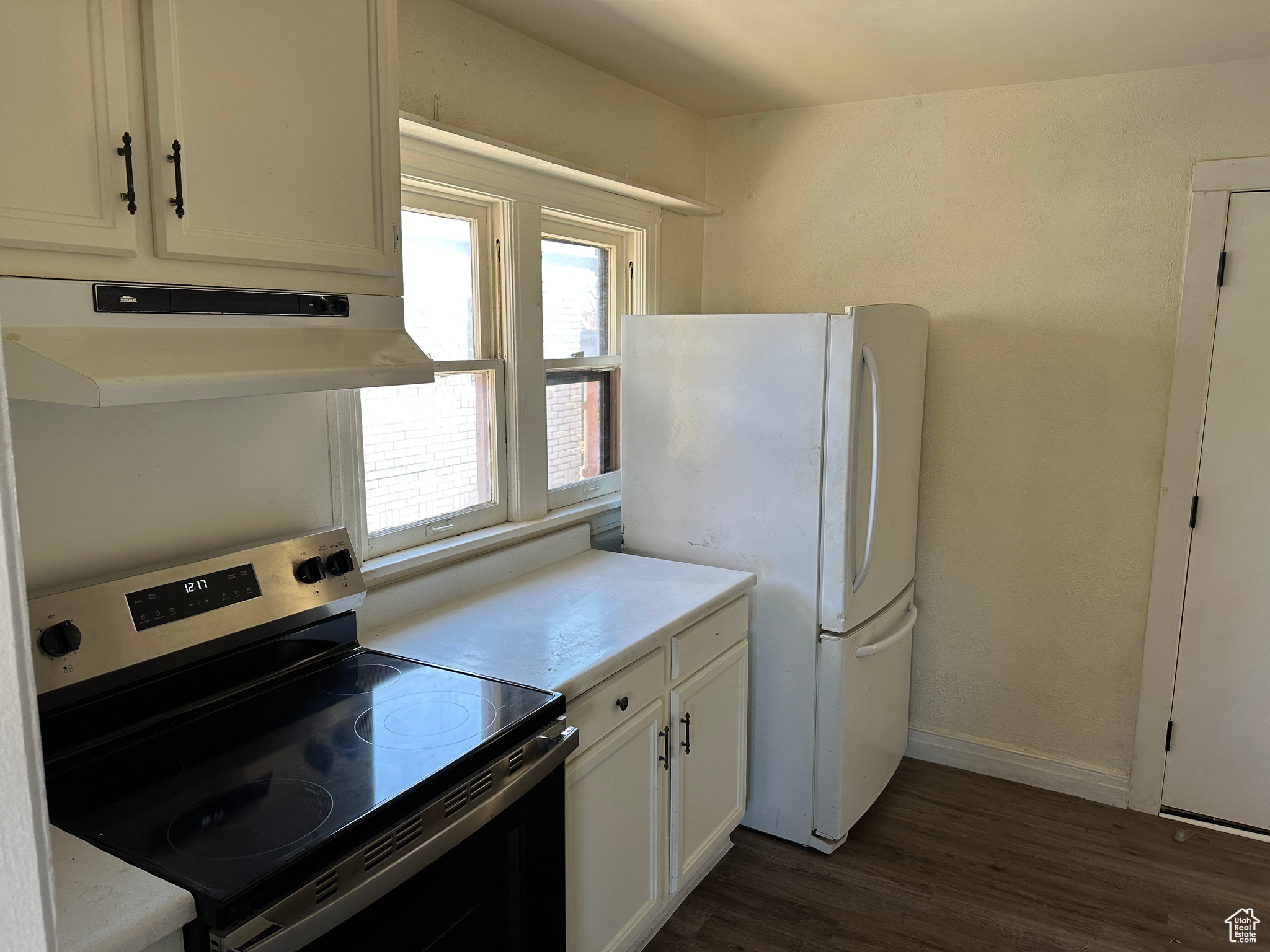 Kitchen featuring white cabinets, dark hardwood / wood-style floors, stainless steel electric stove, and white fridge