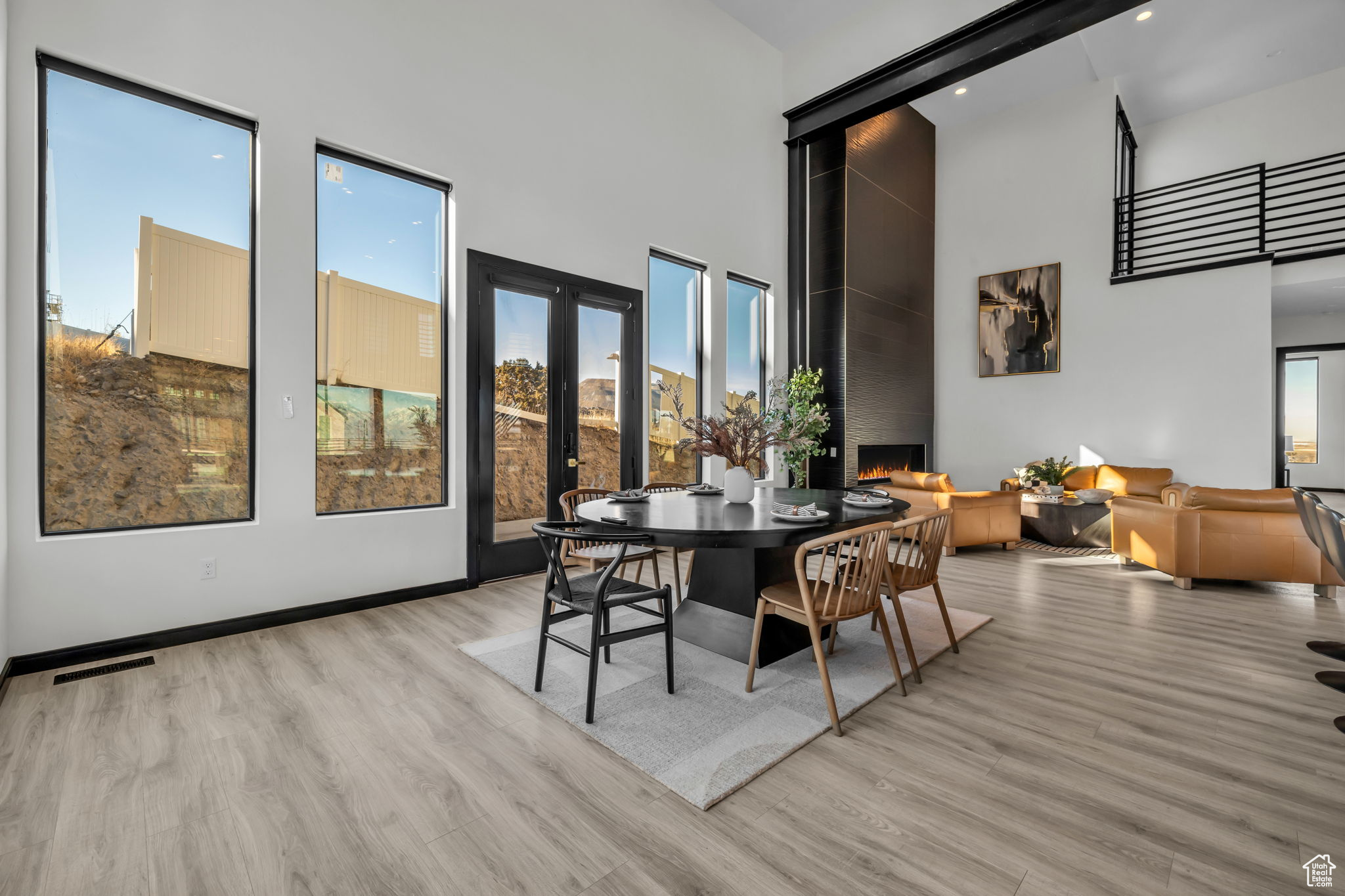 Dining area featuring light wood-type flooring, french doors, a towering ceiling, and a large fireplace