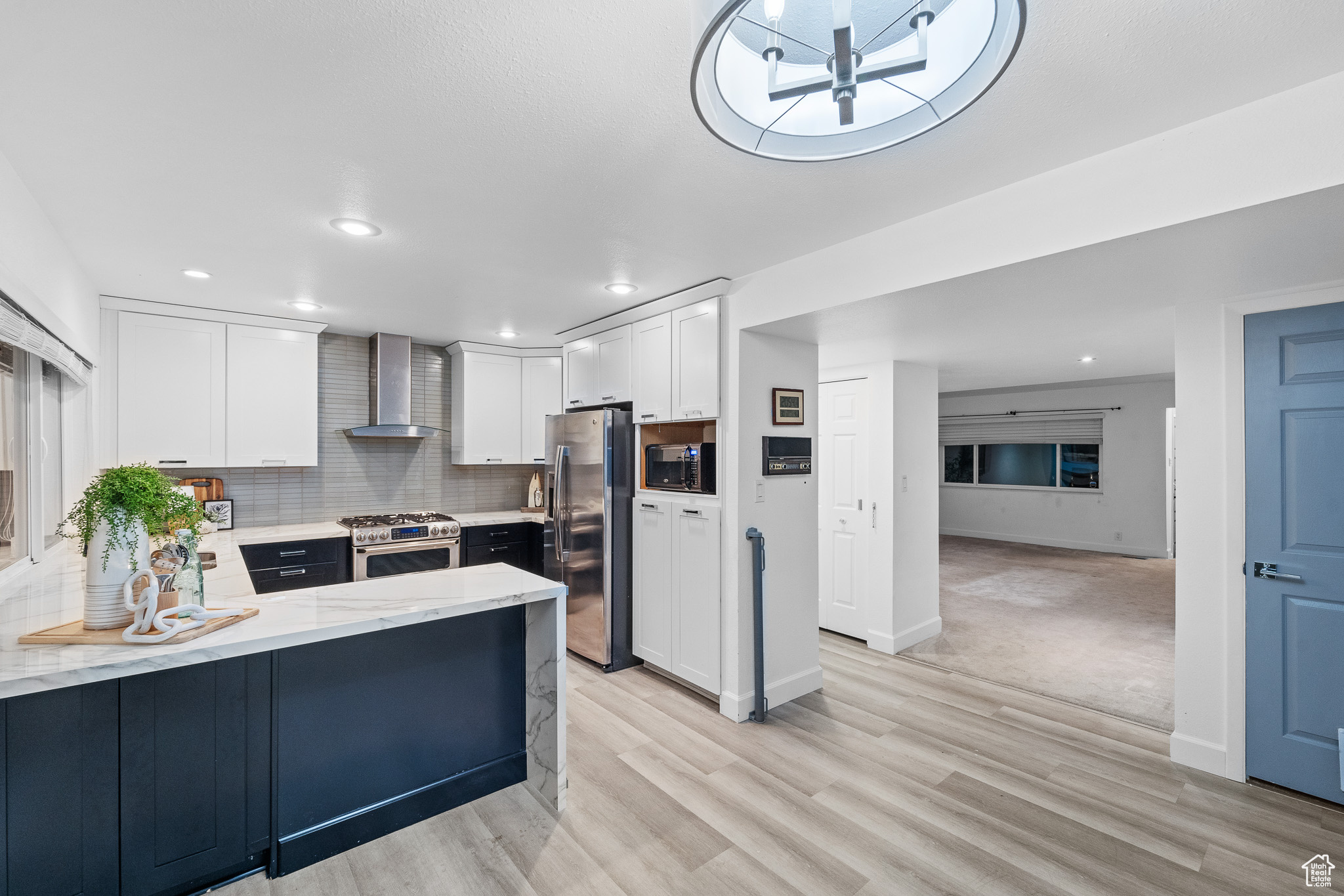 Kitchen featuring decorative backsplash, appliances with stainless steel finishes, wall chimney range hood, white cabinets, and light hardwood / wood-style floors