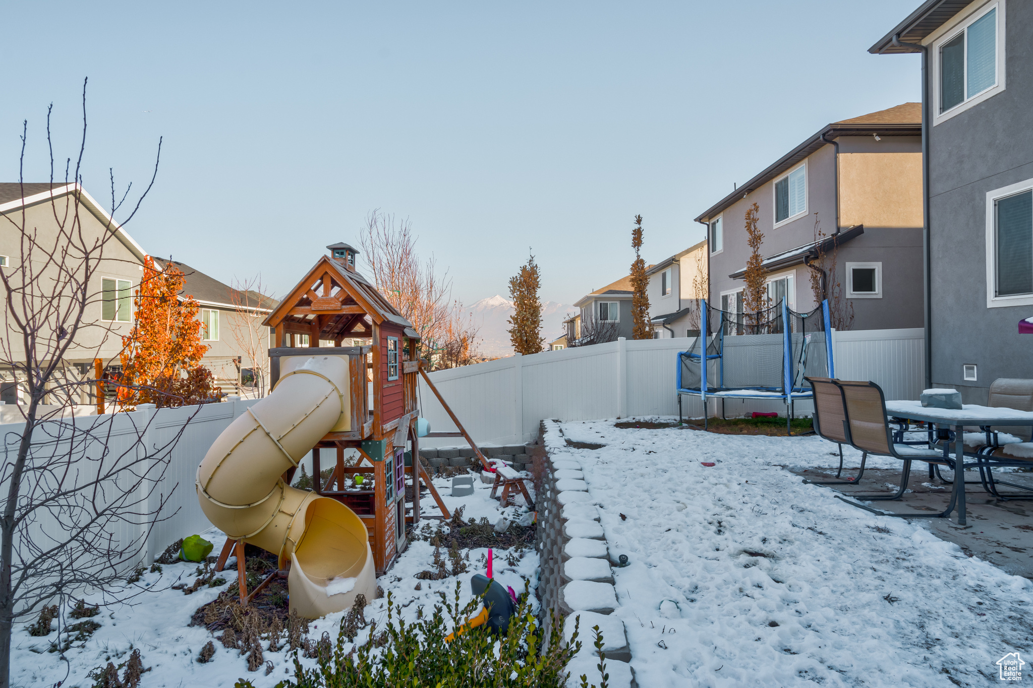 Yard layered in snow with a playground and a trampoline